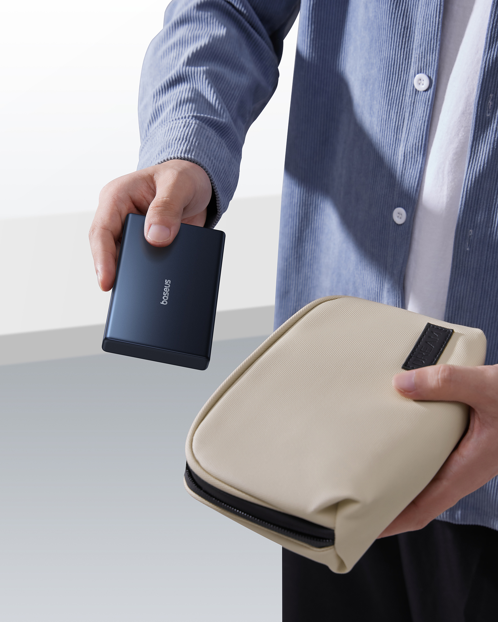Bir kişi koyu mavi bir Baseus powerbank ve bej bir çanta tutuyor. Kişi mavi kadife bir gömlek giyiyor.