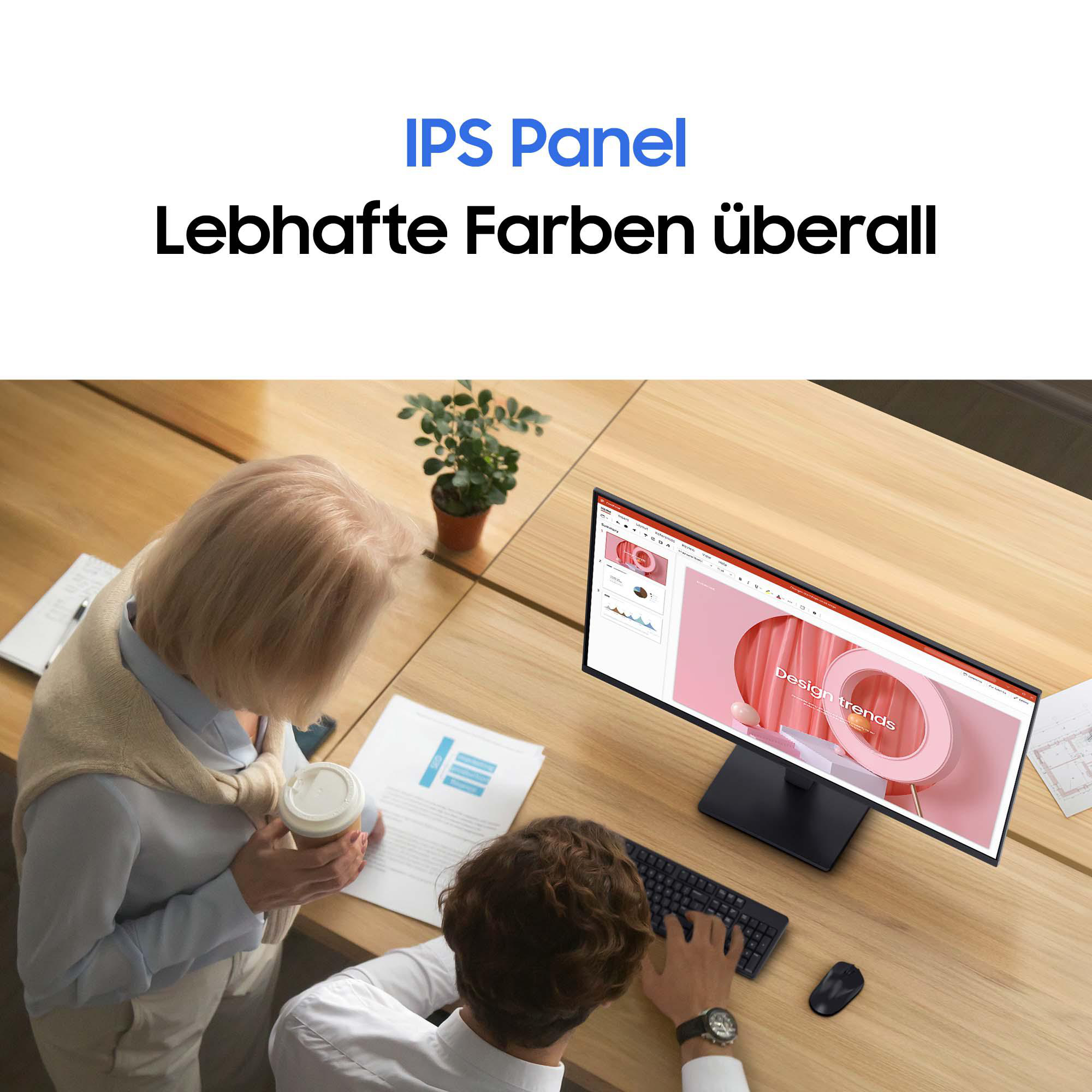 Zwei Personen an einem Schreibtisch mit einem Monitor, der ein rosa Design anzeigt. Einer hält Kaffee, der andere tippt. Text oben.