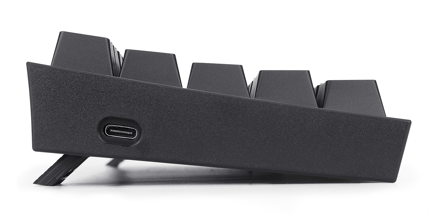 Widok z boku czarnej klawiatury. Widoczny port USB-C. Klawisze są czarne. Jedna nóżka jest wysunięta do podniesienia.