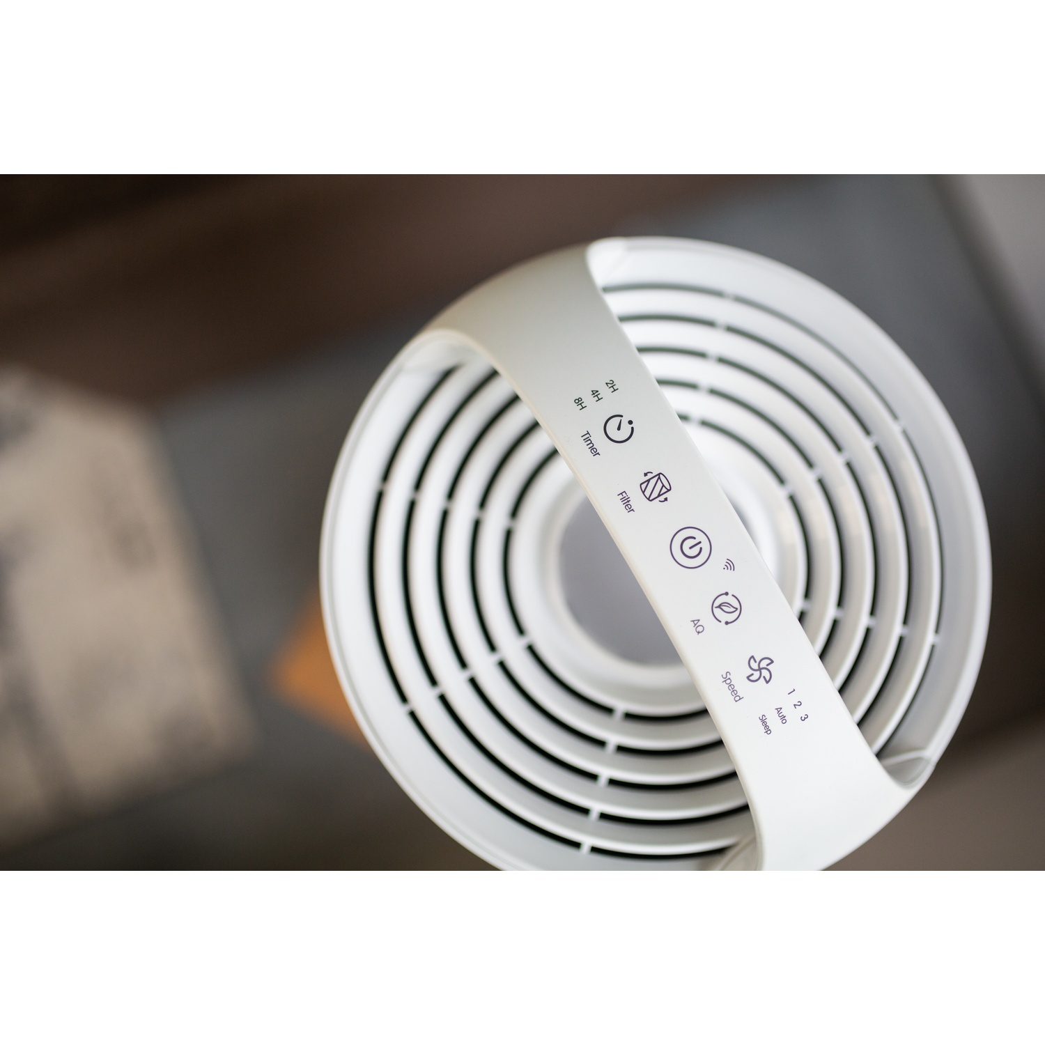 Top view of a white air purifier. It has a handle with control buttons. The purifier has circular vents.