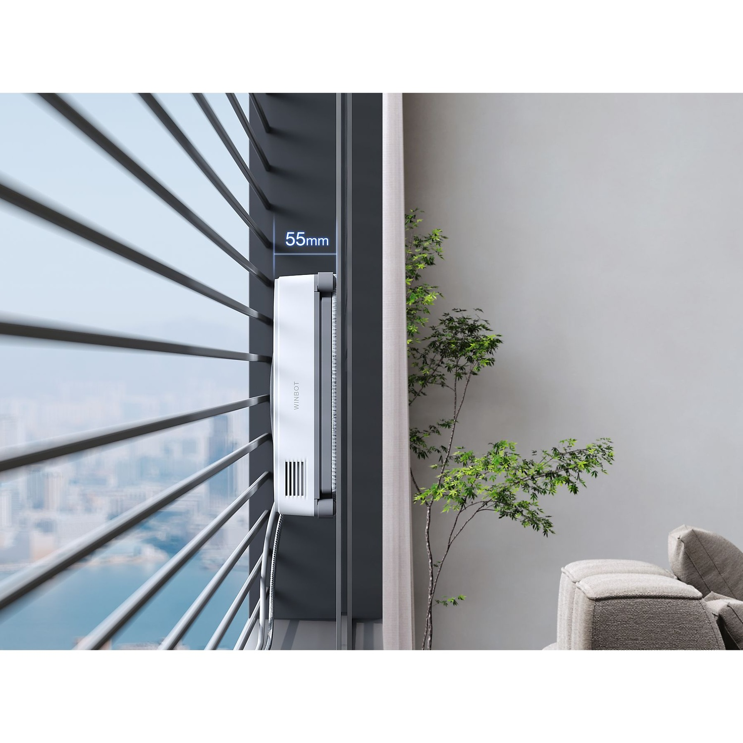 A white Winbot device is mounted on a window. A tree with green leaves is on the right. The window has blinds with city view.