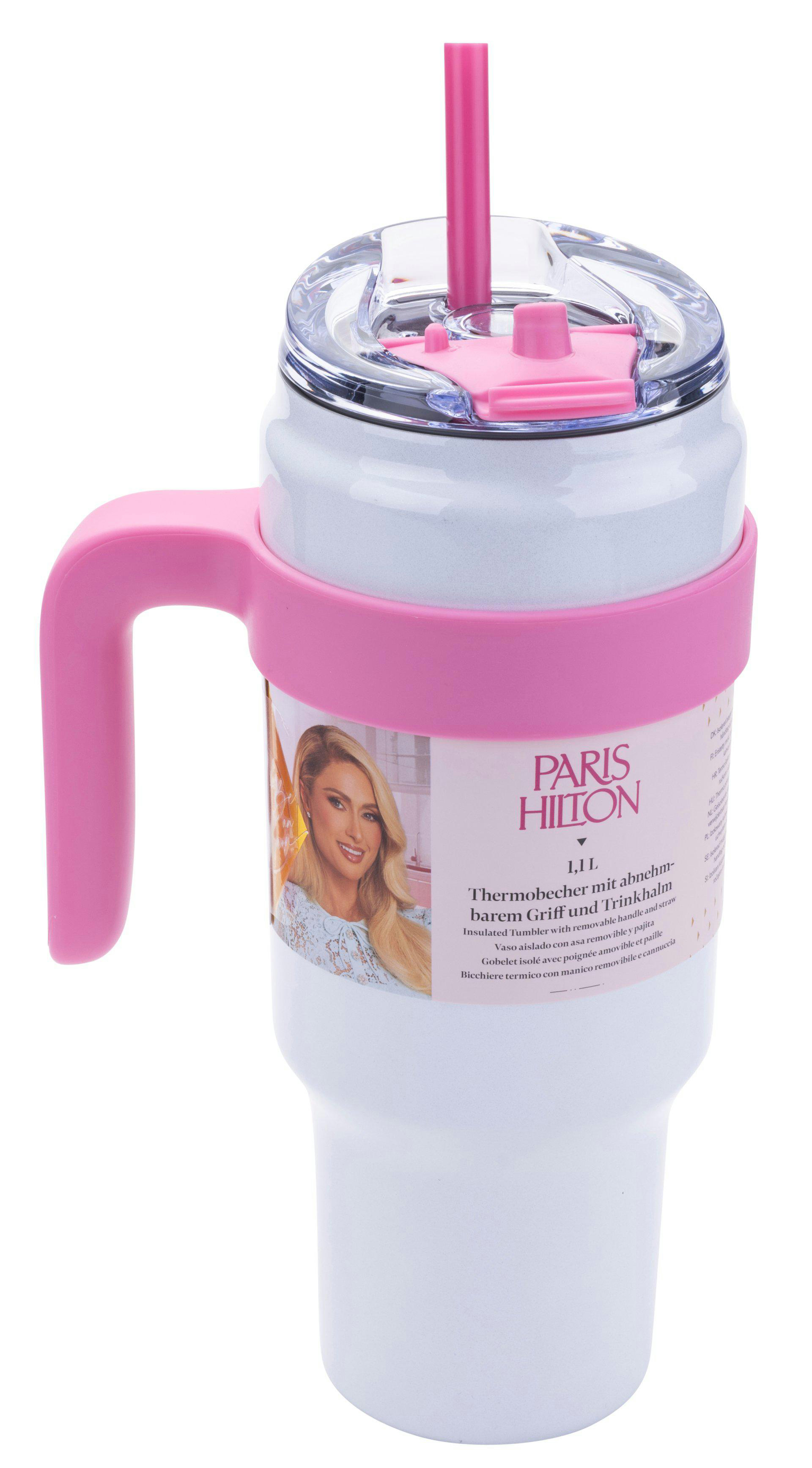 Ein weißer Becher mit rosa Griff, Band und Strohhalm. Er hat einen durchsichtigen Deckel. Das Etikett zeigt Paris Hilton.