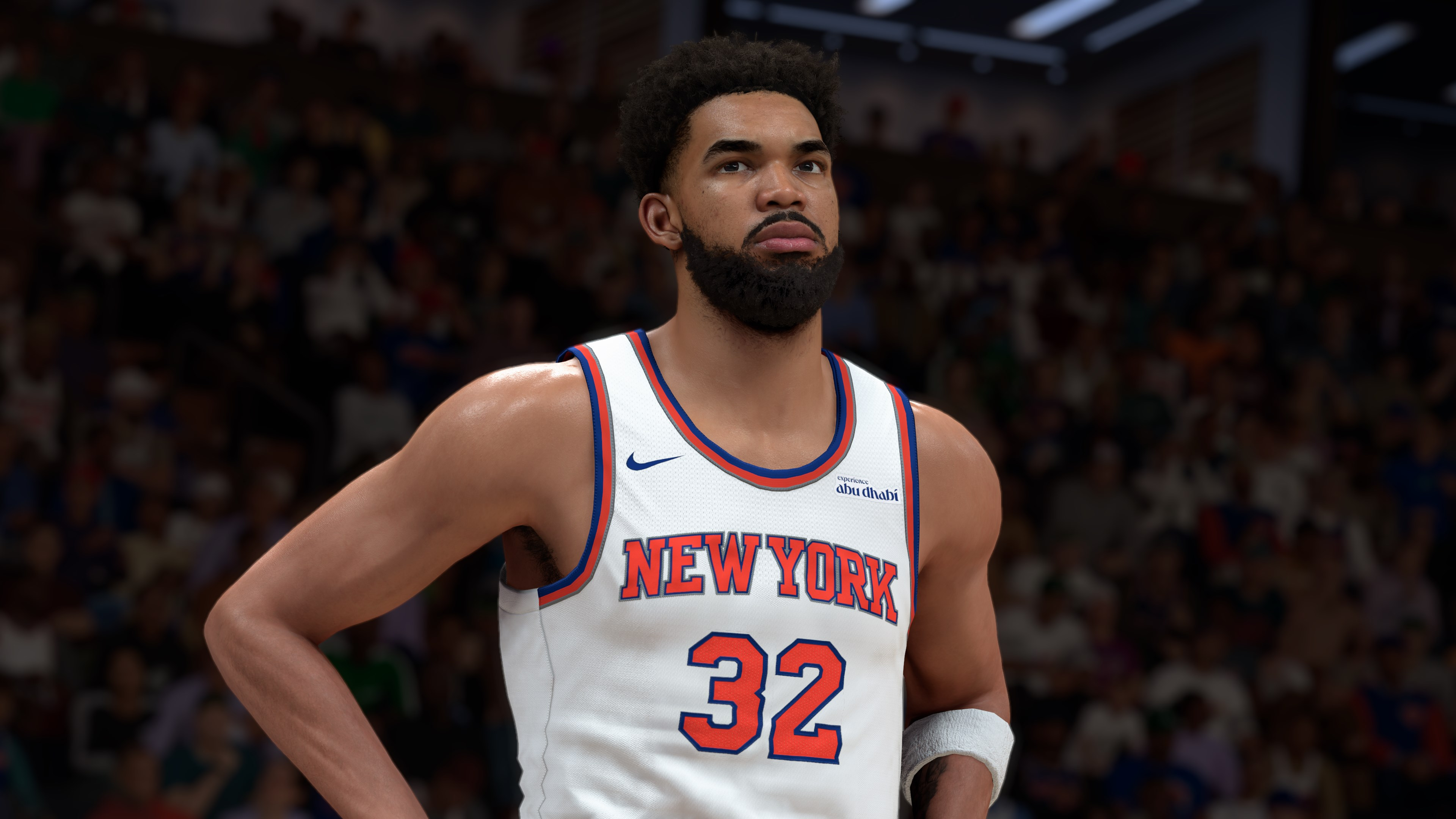Un giocatore di basket con la maglia dei Knicks guarda in alto. La maglia è bianca con dettagli arancioni e blu. Lo sfondo è una folla.