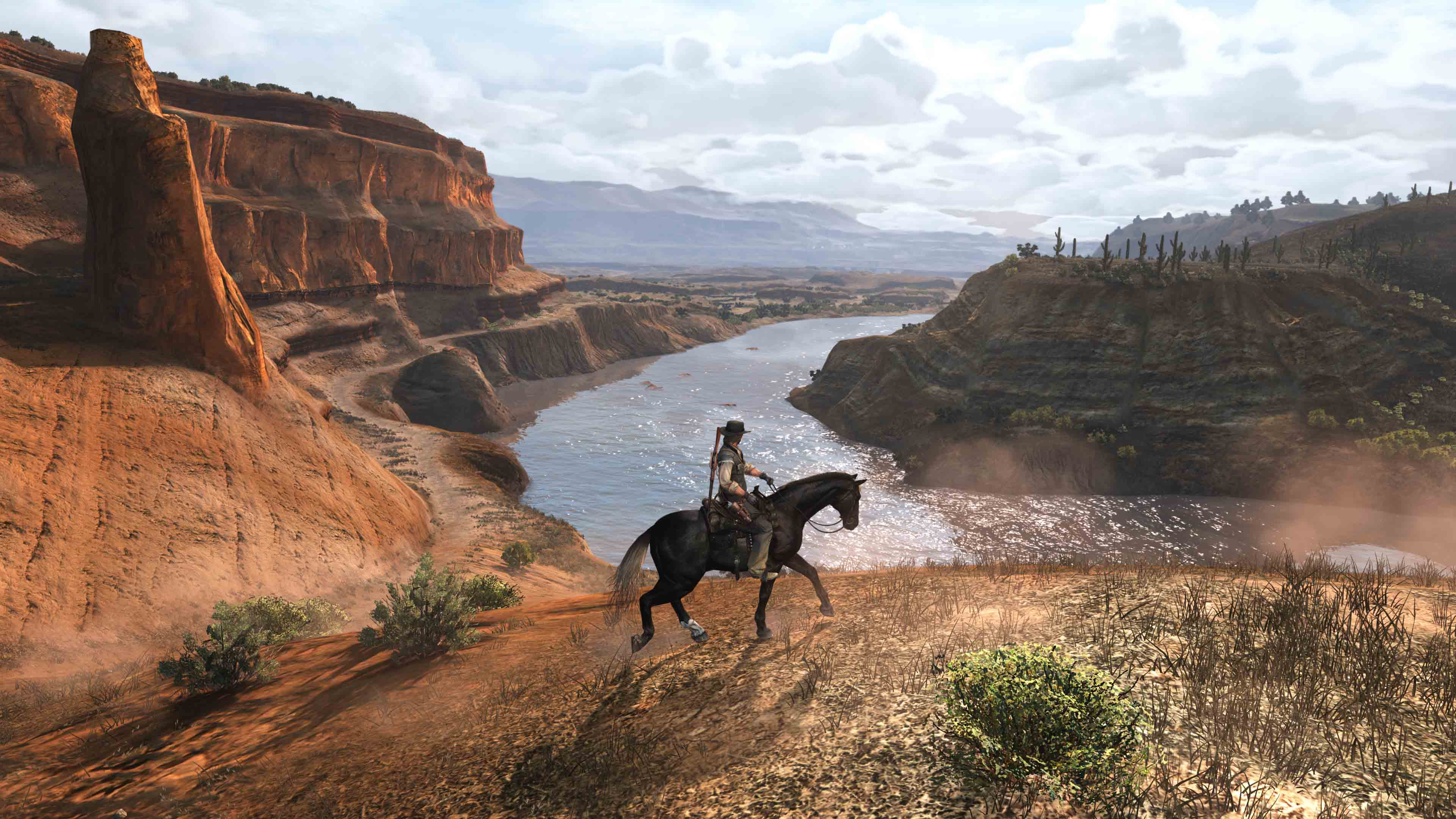 Una persona su un cavallo nero cavalca lungo un fiume in un canyon. Scogliere di roccia rossa e un paesaggio desertico sono visibili sullo sfondo.