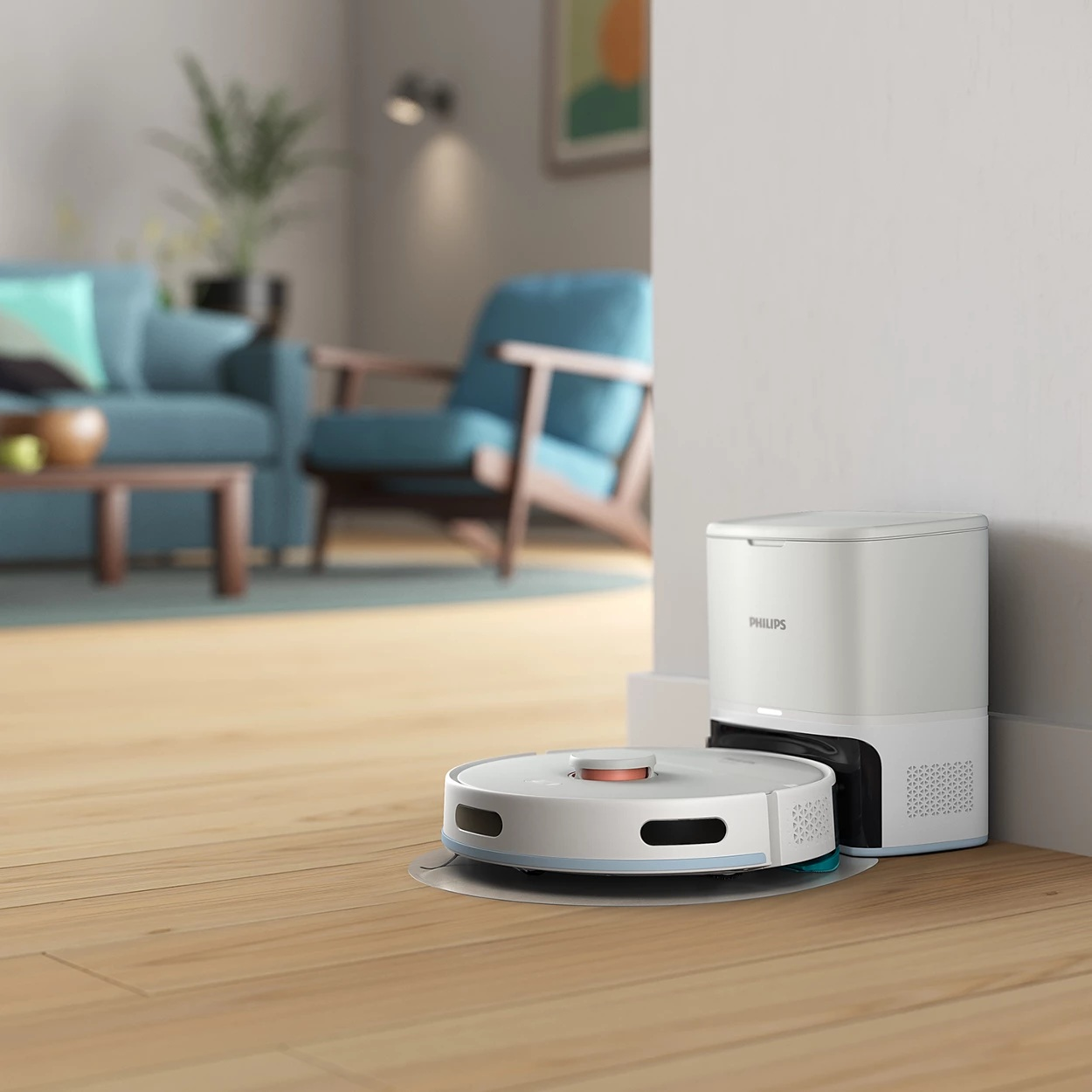 Biały odkurzacz automatyczny i stacja ładująca na tle białej ściany. Niebieska sofa i krzesło w tle.