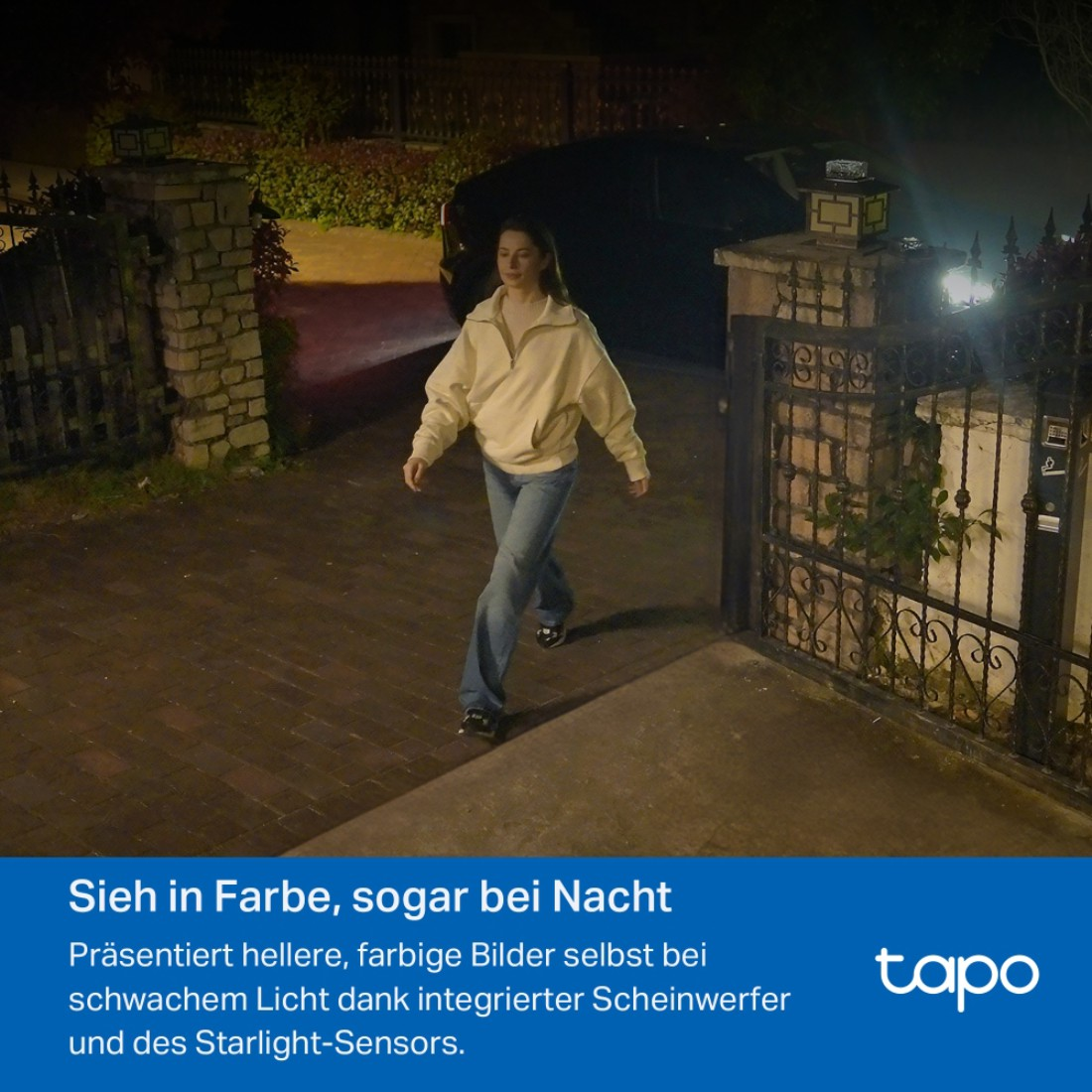 Eine Frau geht nachts auf die Kamera zu und nähert sich einem Tor. Im Hintergrund ist ein Auto geparkt. Die Szene wird von einer Straßenlaterne beleuchtet.