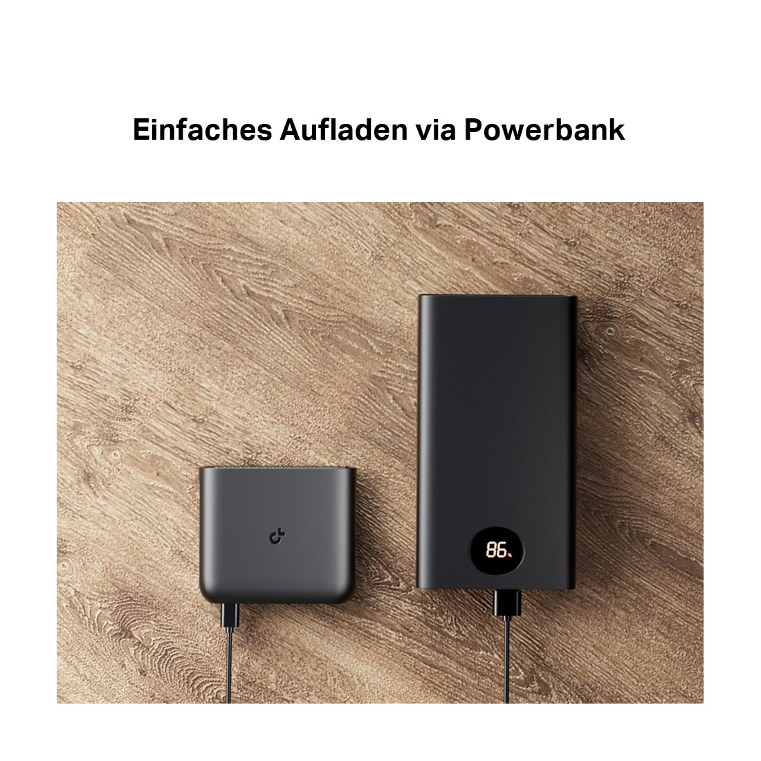 Zwei schwarze Powerbanks auf Holzoberfläche, eine mit Anzeige von 86% Ladung. Beide sind mit schwarzen Kabeln verbunden.