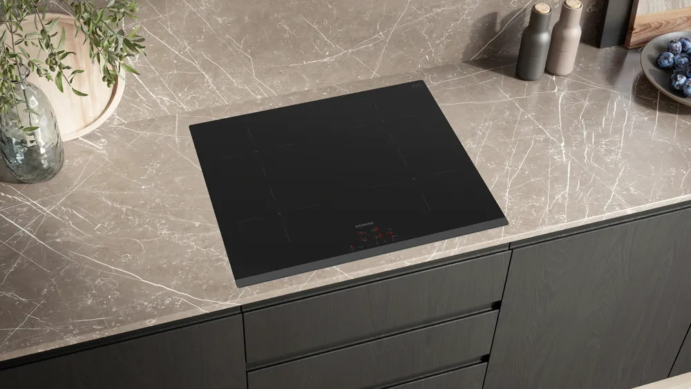 Czarna płyta indukcyjna na marmurowym blacie. Akcesoria kuchenne na blacie. Pod spodem ciemnoszare szafki.