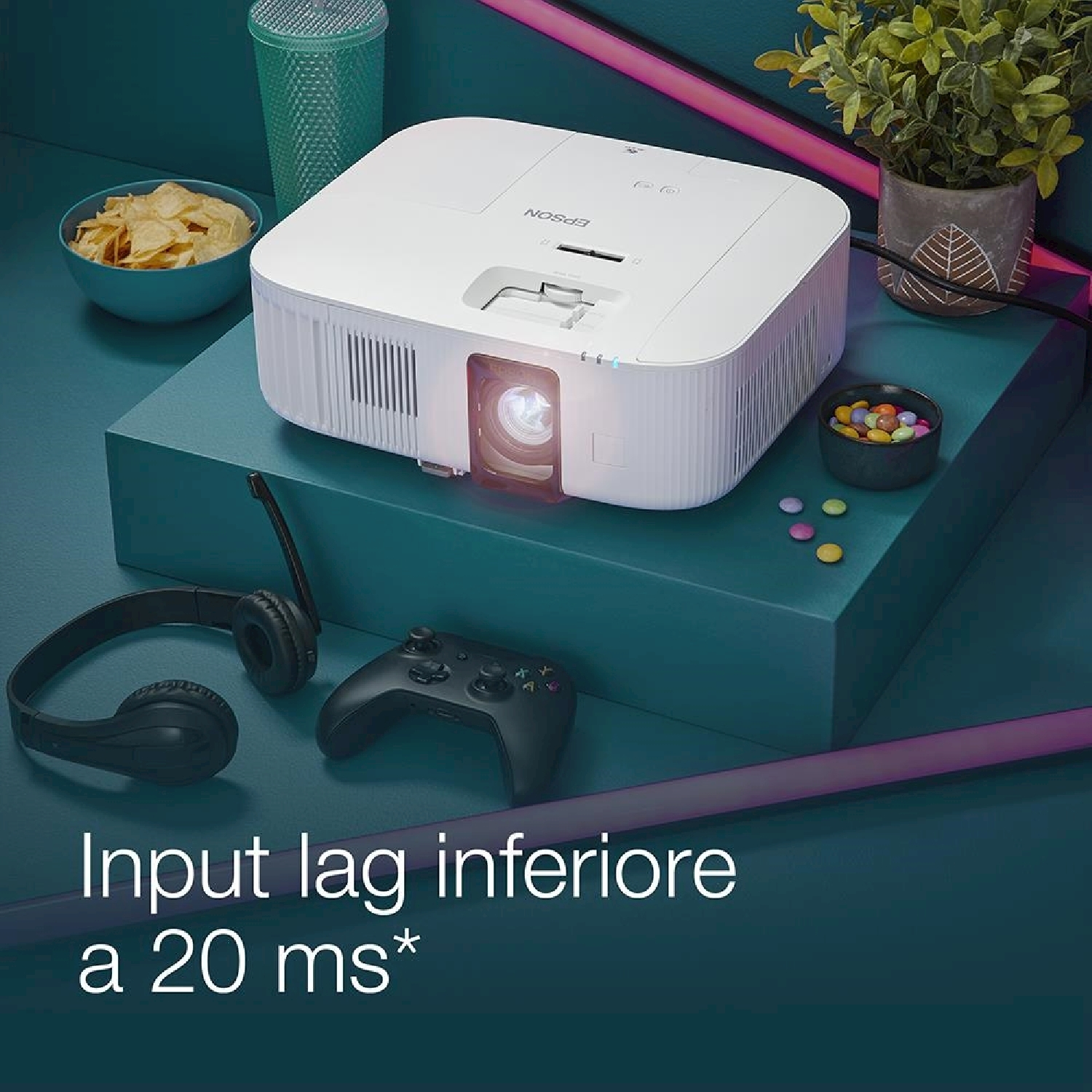 Un proiettore bianco su una piattaforma verde acqua con snack, cuffie e un controller. Testo: 'Input lag inferiore a 20 ms*'.