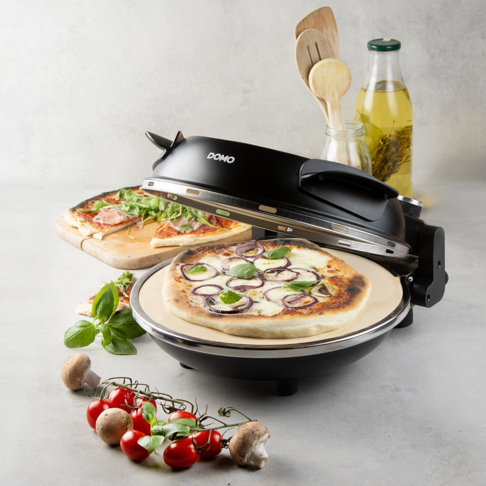 Pizza oven with a pizza on a stone. Ingredients are visible, including basil, tomatoes, and mushrooms. Another pizza is on a wooden board.