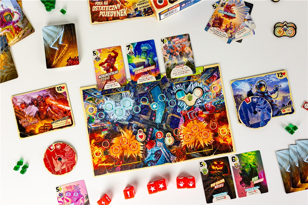 Konfiguracja gry planszowej z kartami, kostkami i żetonami na białej powierzchni. Karty przedstawiają potwory i akcje. Plansza znajduje się w środku.