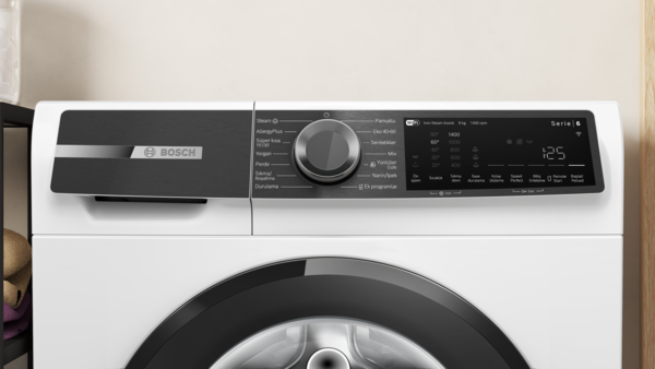 Siyah kontrol panelli beyaz bir Bosch çamaşır makinesi. Bir kadranı, dijital ekranı ve çeşitli program seçenekleri var.