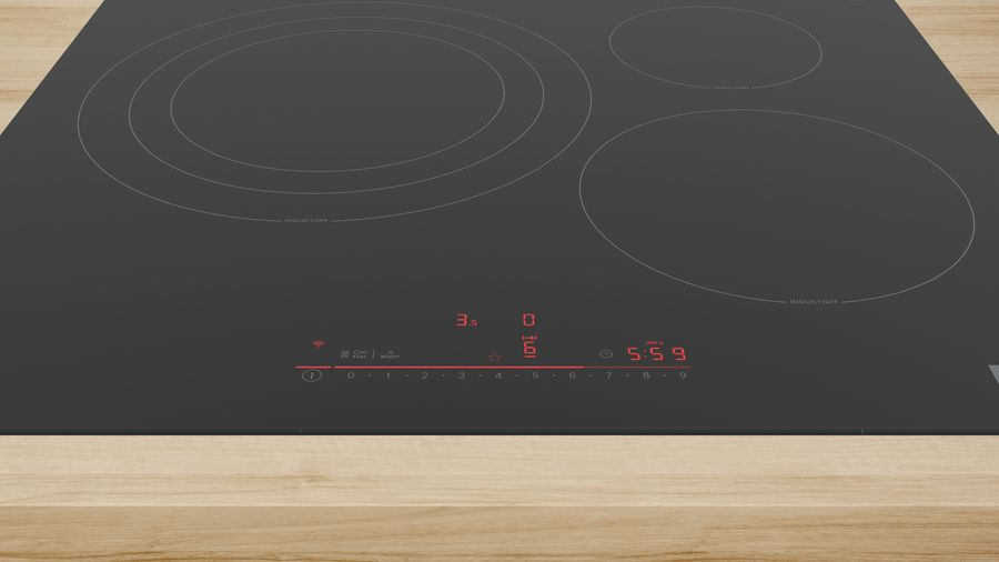 Placa de inducción negra con cuatro zonas de cocción y pantalla digital roja. Superficie de madera debajo.