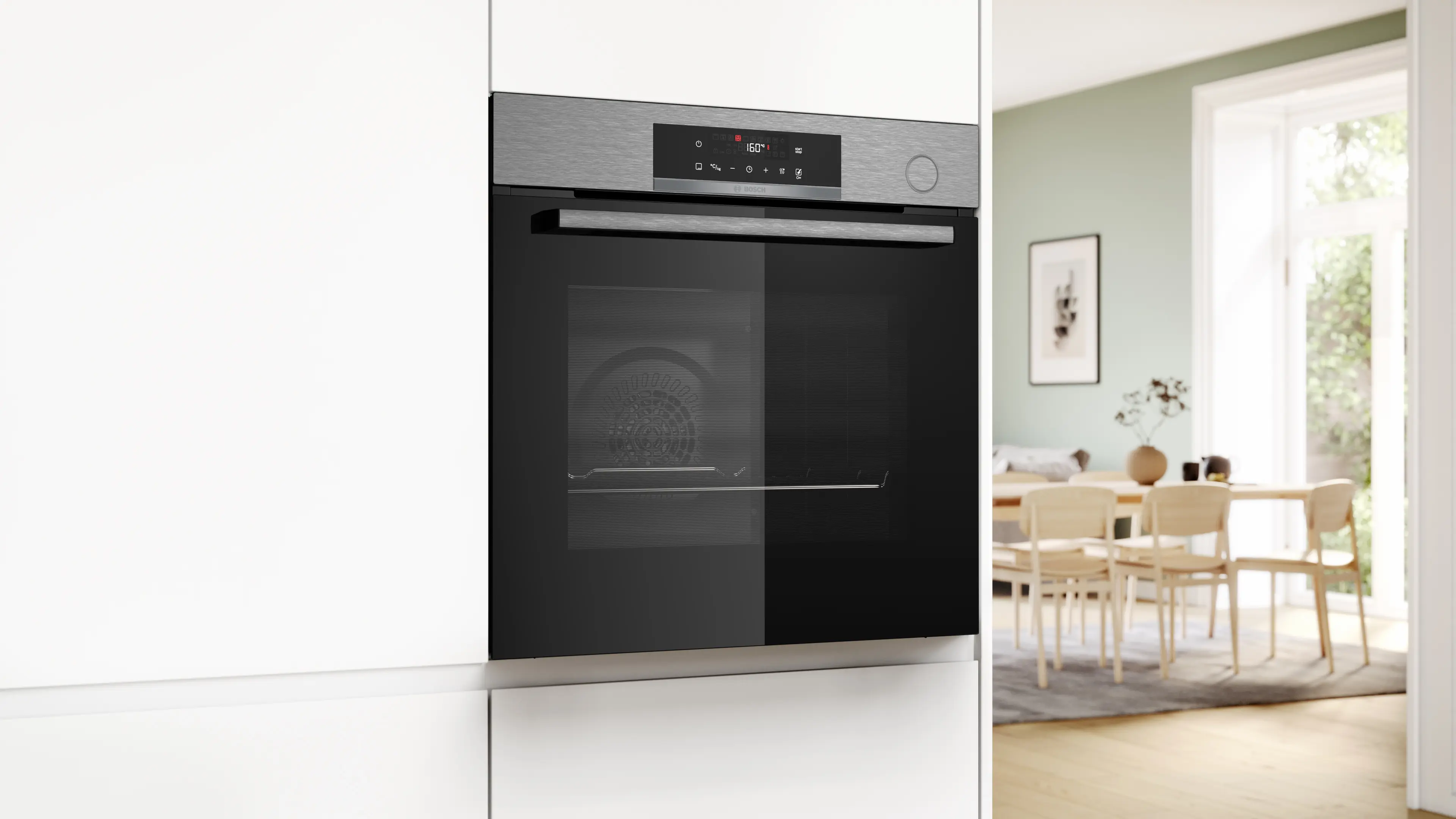 Un horno está integrado en un armario blanco. La pantalla del horno muestra 160 grados. A la derecha se ve un comedor.