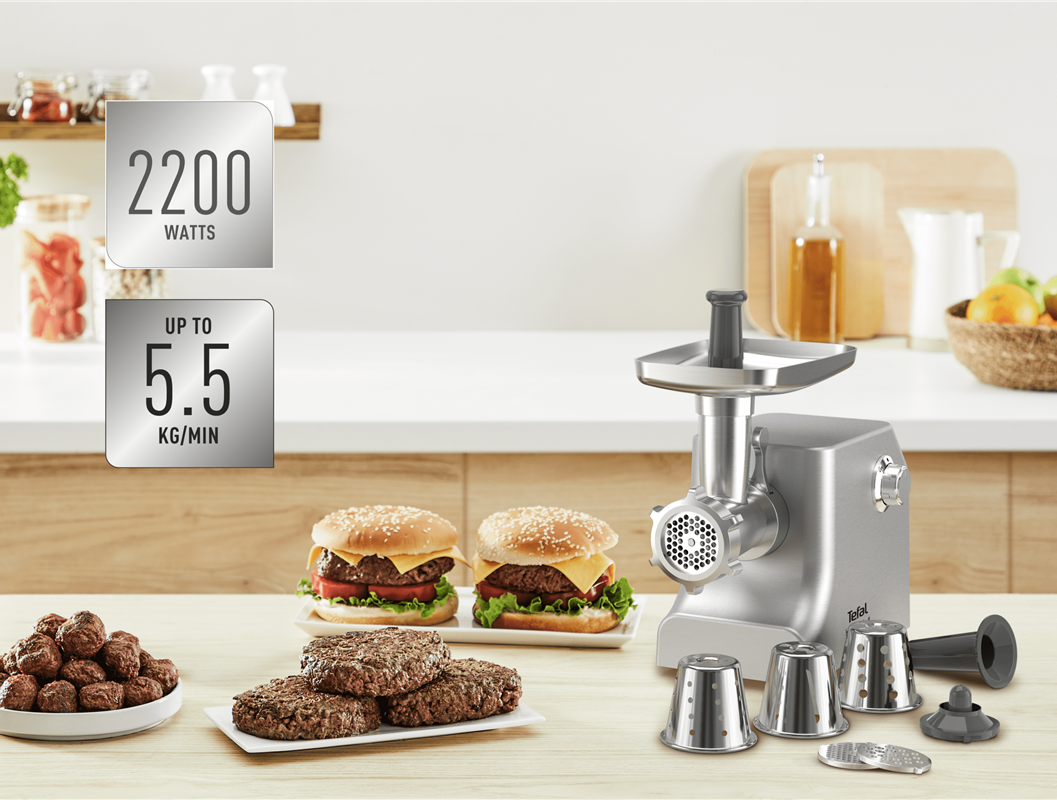 Húsdaráló tartozékokkal, hamburgerekkel és húsgombócokkal egy faasztalon. Az információs táblák 2200 wattot és 5,5 kg/percet mutatnak.
