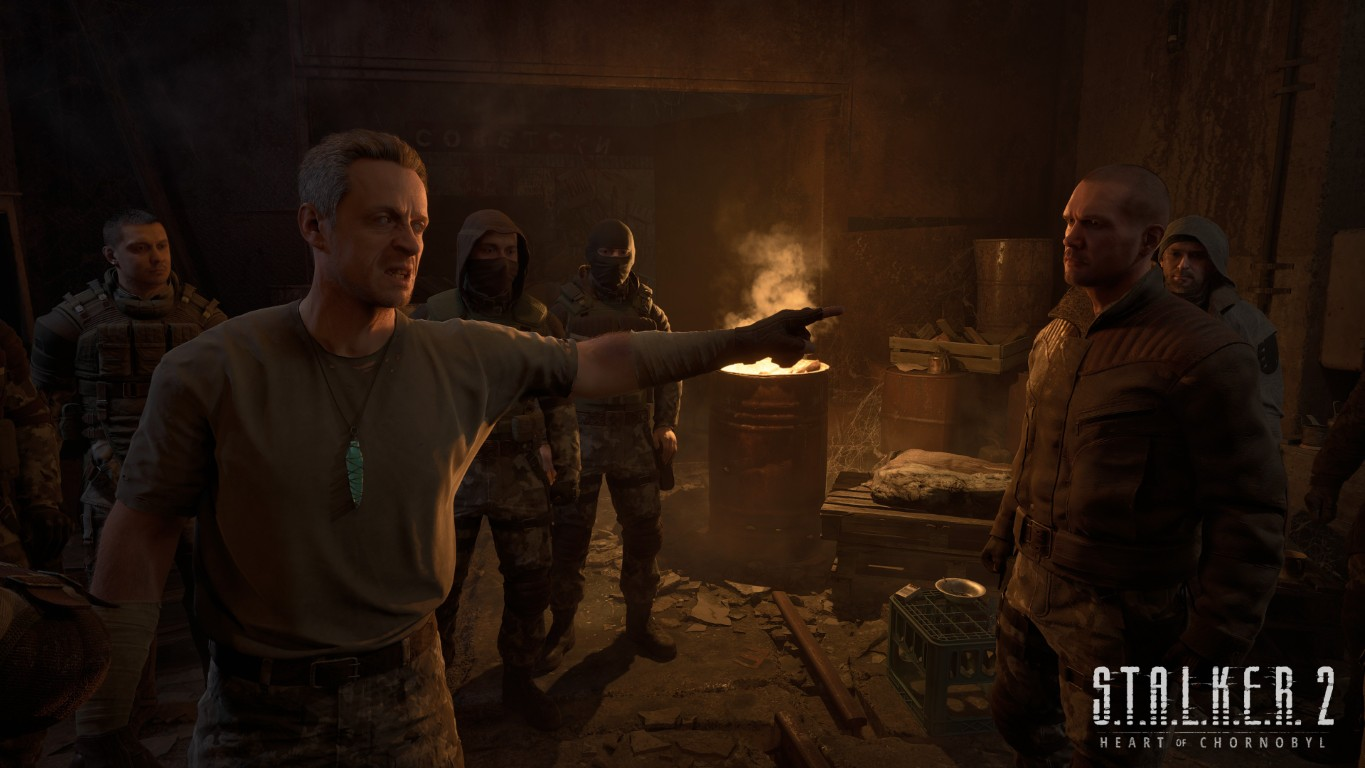 Mężczyzna wskazuje palcem, zwracając się do innych w słabo oświetlonym pomieszczeniu. Inni stoją wokół beczki z ogniem. Logo gry widoczne w prawym dolnym rogu.
