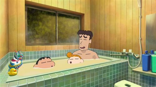 Una familia en una bañera. Un hombre y dos niños se bañan en el agua. Hay una ventana al fondo y un juguete al lado.