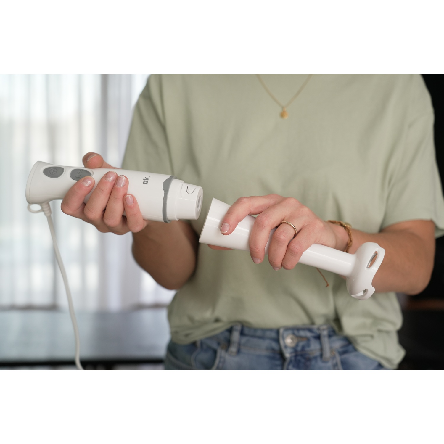 Una persona collega un frullatore a immersione bianco. Tiene il motore e l'accessorio.
