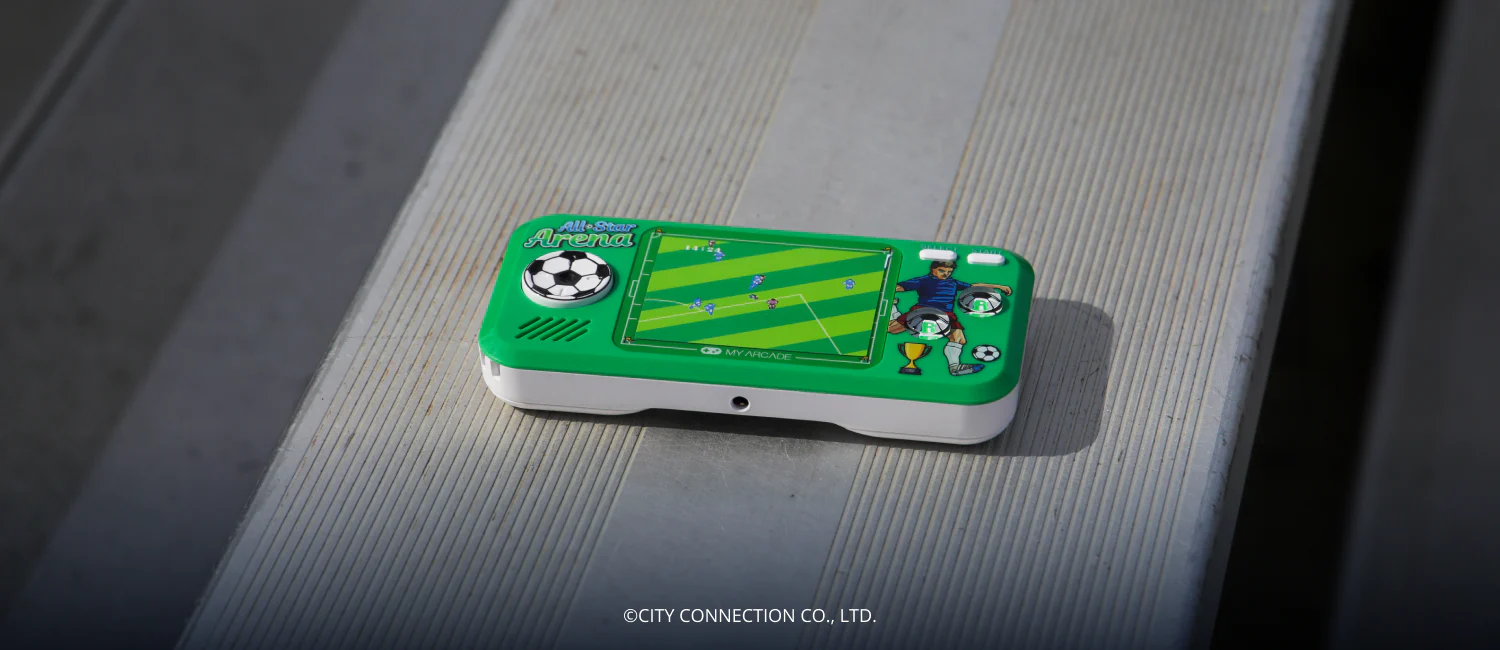 Une console de jeu portable verte et blanche sur le thème du football est posée sur une surface grise. L'écran affiche un jeu de football.