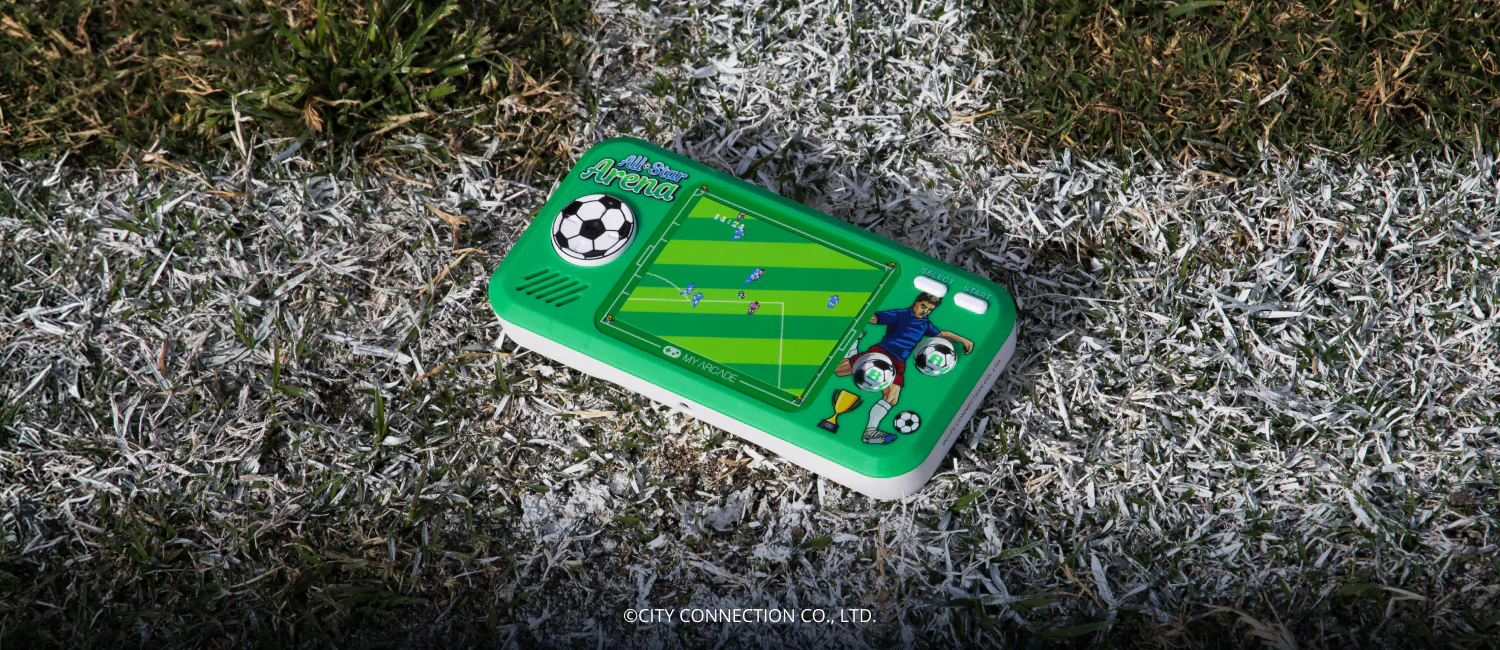 Une console de jeu vidéo portable rétro verte, représentant un match de football, repose sur de l'herbe. Des lignes blanches délimitent le terrain.