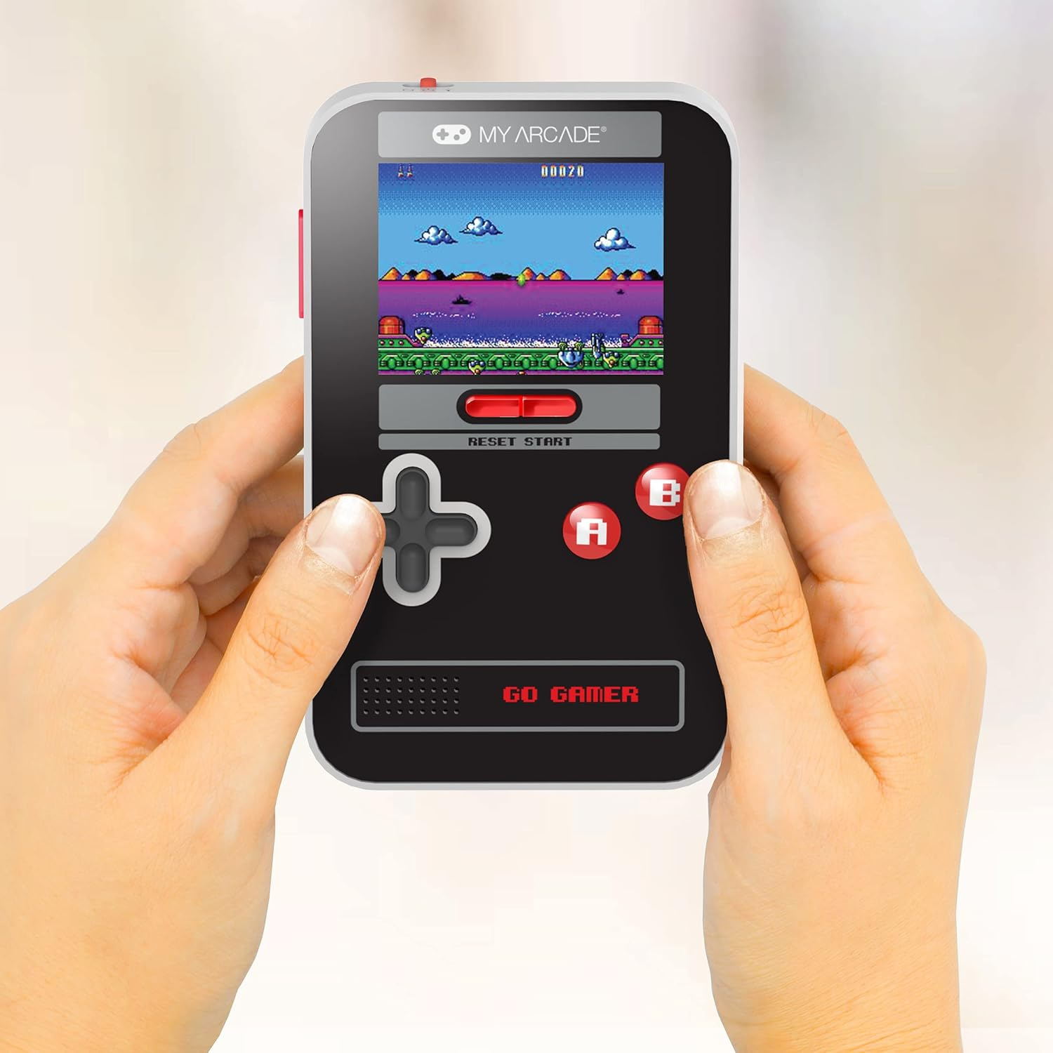Mains tenant une console de jeu portable rétro avec un jeu affiché. La console est noire, avec des boutons rouges et une croix directionnelle.
