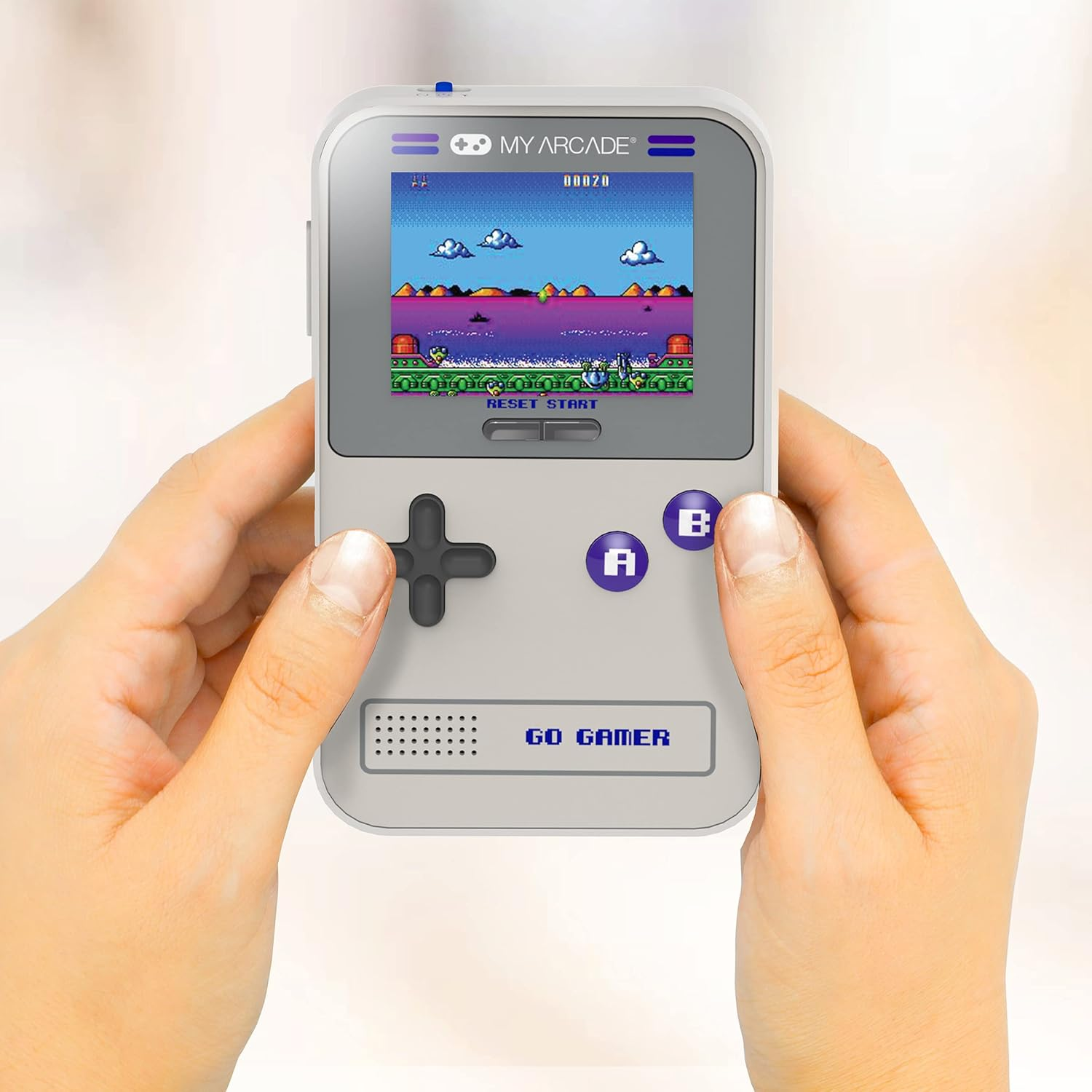 Mains tenant une My Arcade Go Gamer. L'écran affiche une scène de jeu rétro. Boutons : A, B, start et un D-pad.