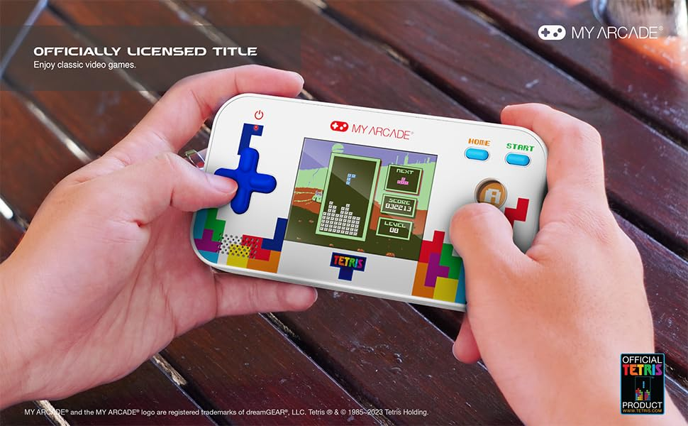 Mains tenant une console de jeu Tetris. L'écran affiche le jeu. Les boutons comprennent une croix directionnelle, début, accueil et le bouton A.