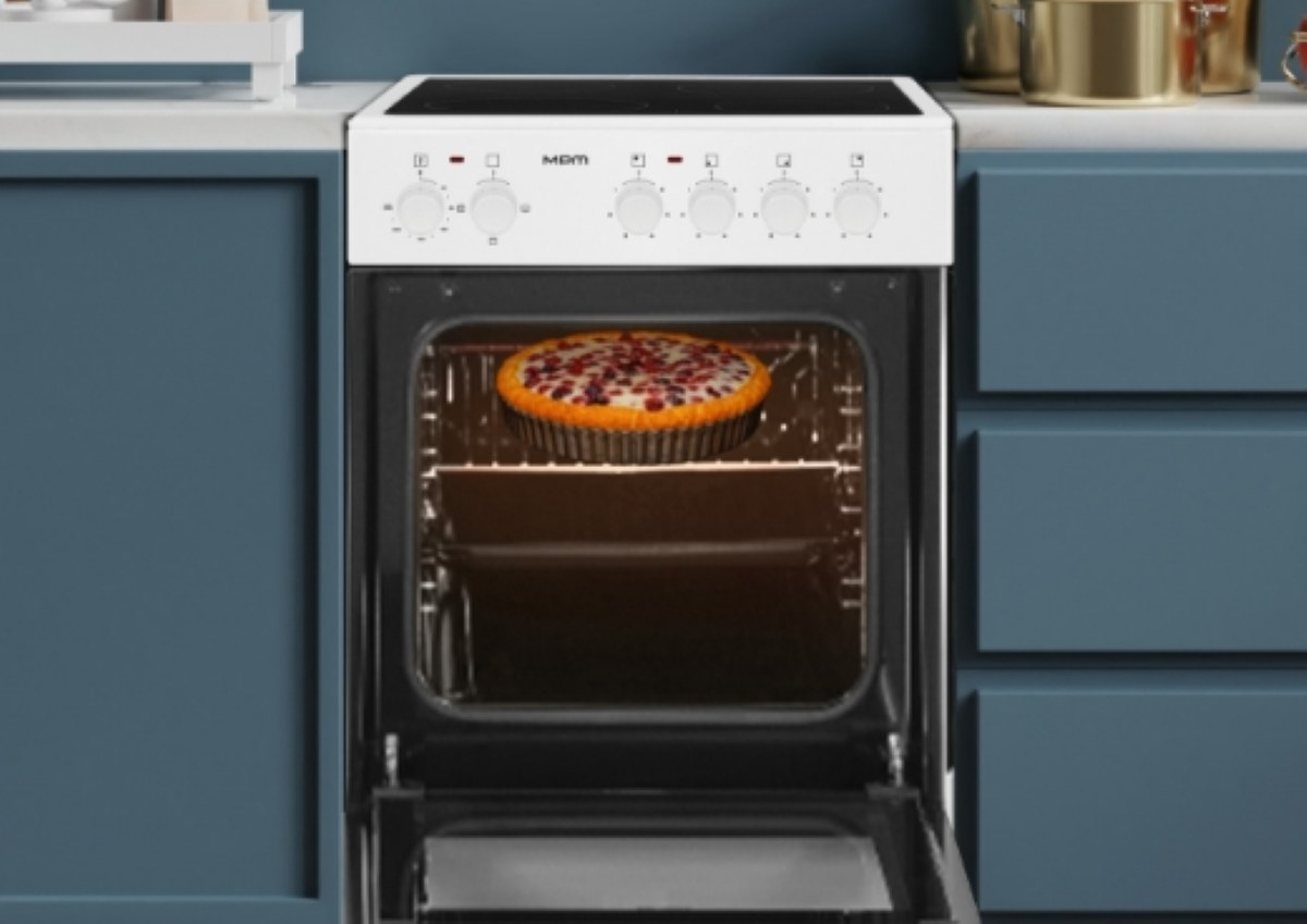 Piekarnik z otwartymi drzwiami. W środku piecze się ciasto. Piekarnik jest biały z czarnymi elementami. Niebieskie szafki go otaczają.