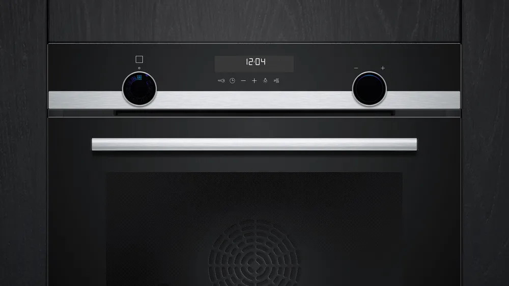 Czarny piekarnik z cyfrowym wyświetlaczem zegara, dwoma pokrętłami i srebrnym uchwytem. Jest 12:04.