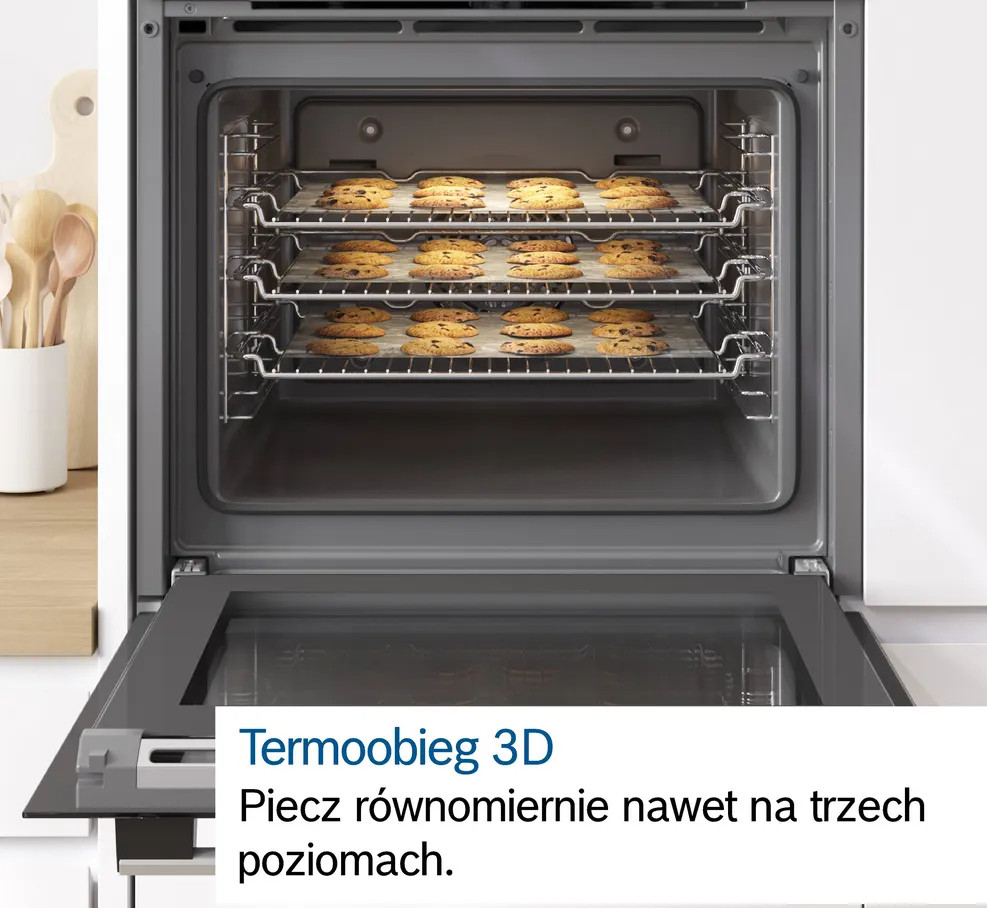 Piekarnik z trzema rusztami ciasteczek do pieczenia. Drzwi piekarnika są otwarte. Tło pokazuje przybory kuchenne na blacie.