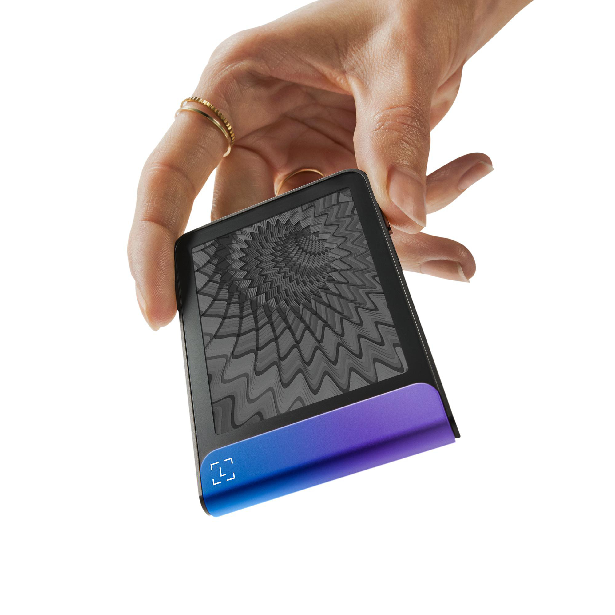 Eine Hand hält ein schwarzes Gerät mit blau-violettem Farbverlauf. Der Bildschirm zeigt ein graues Spiralmuster. Goldringe schmücken die Finger.