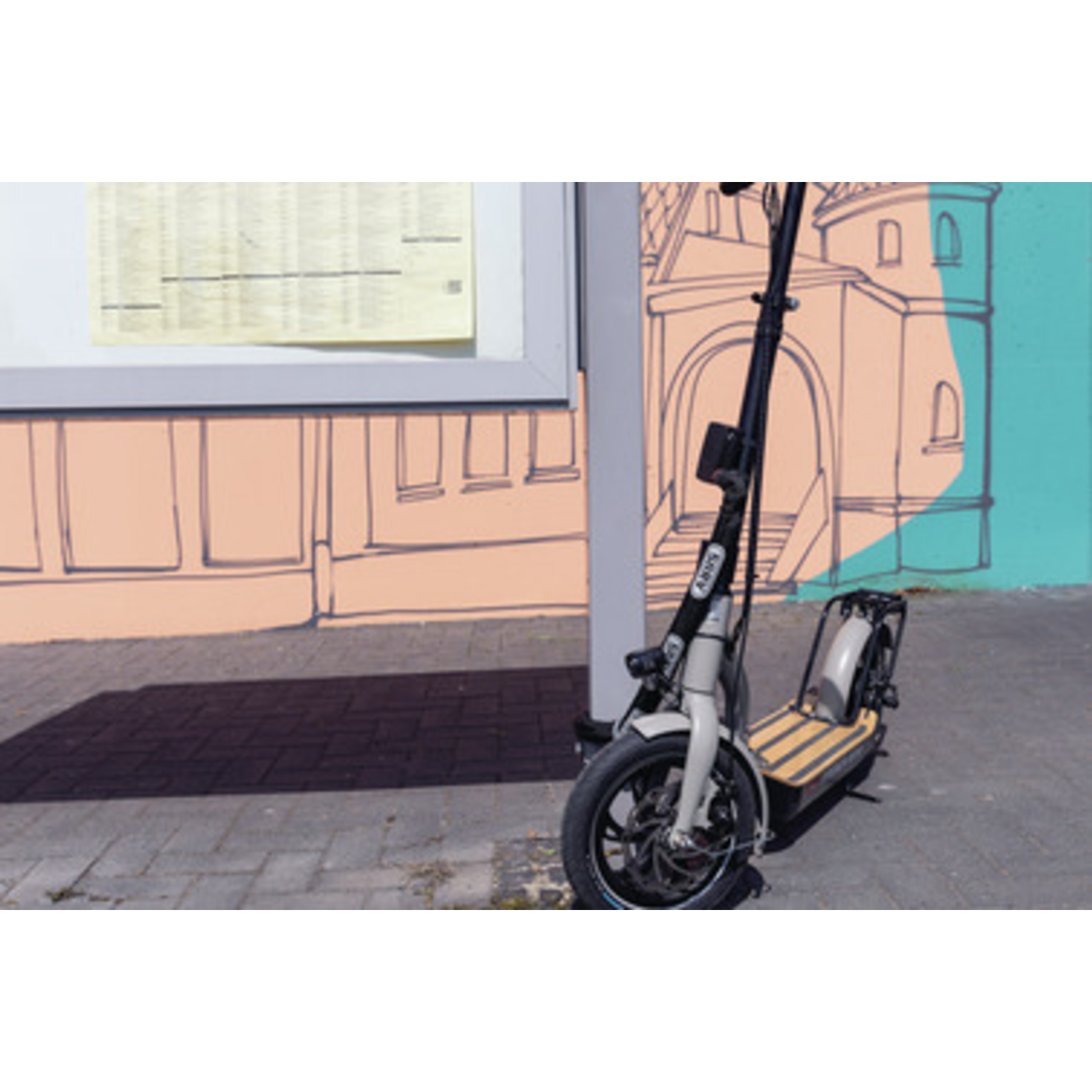 Electric scooter parked on a brick path. In the background a mural of a building and a sign.