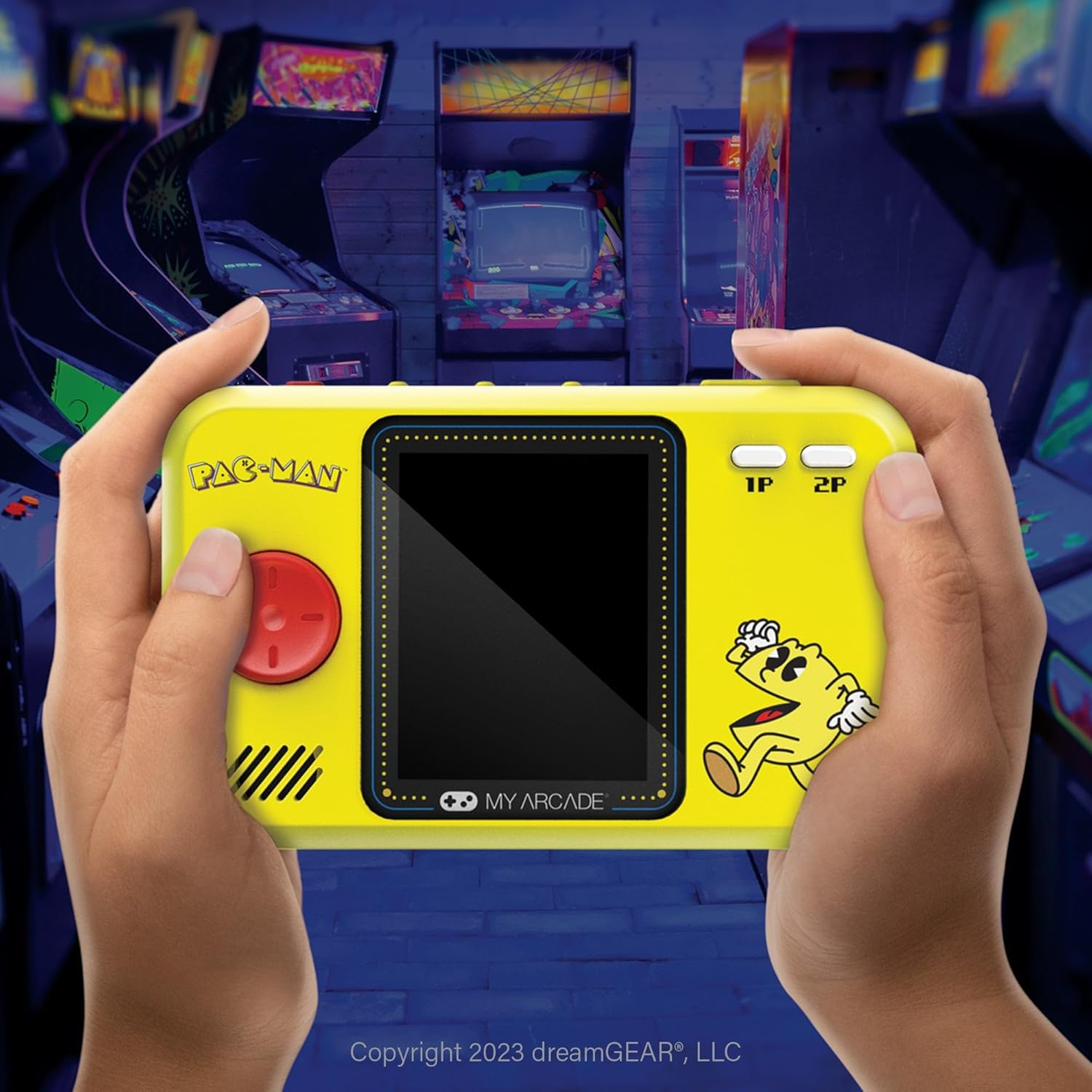 Mains tenant une console de jeu portable Pac-Man jaune. Des bornes d'arcade sont en arrière-plan. L'écran est noir. Personnage de Pac-Man à droite.
