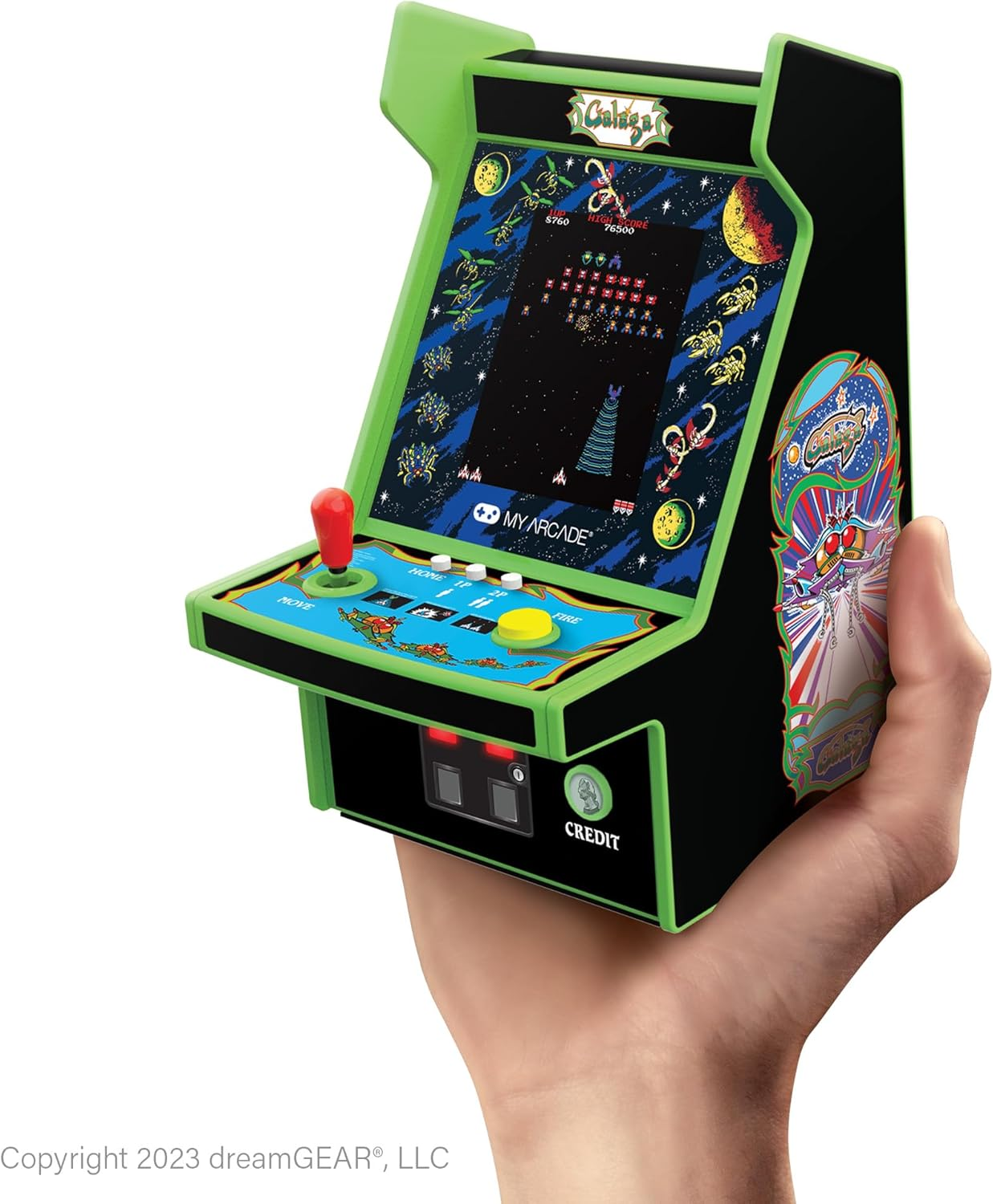 Ein Miniatur-Arcade-Spiel wird in der Hand gehalten. Es zeigt einen 'Galaga'-Bildschirm, einen roten Joystick und eine 'CREDIT'-Taste. Das Spiel ist grün und schwarz.
