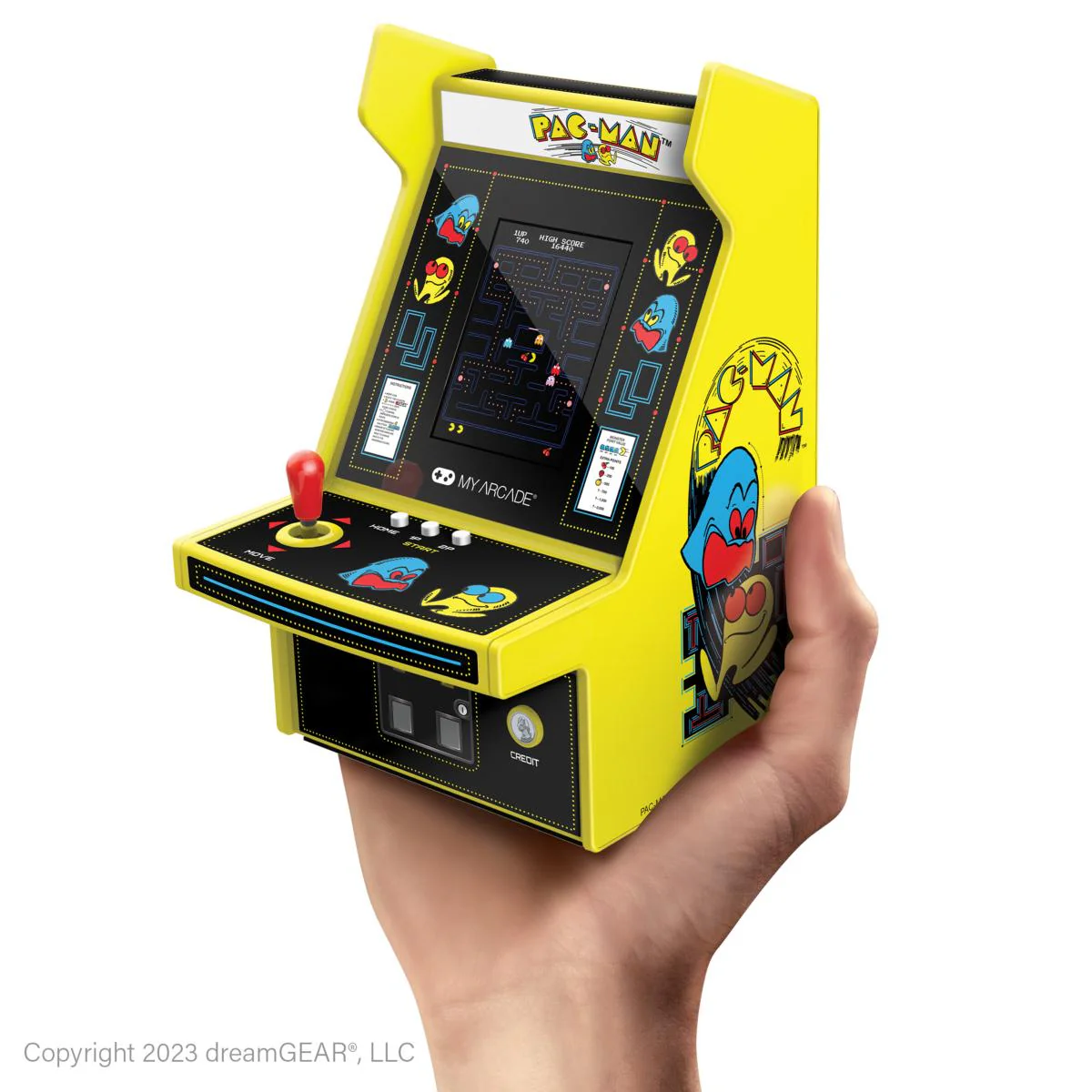 Une borne d'arcade Pac-Man miniature tenue dans une main. Elle est jaune et noire, avec le logo Pac-Man. L'écran affiche le jeu.