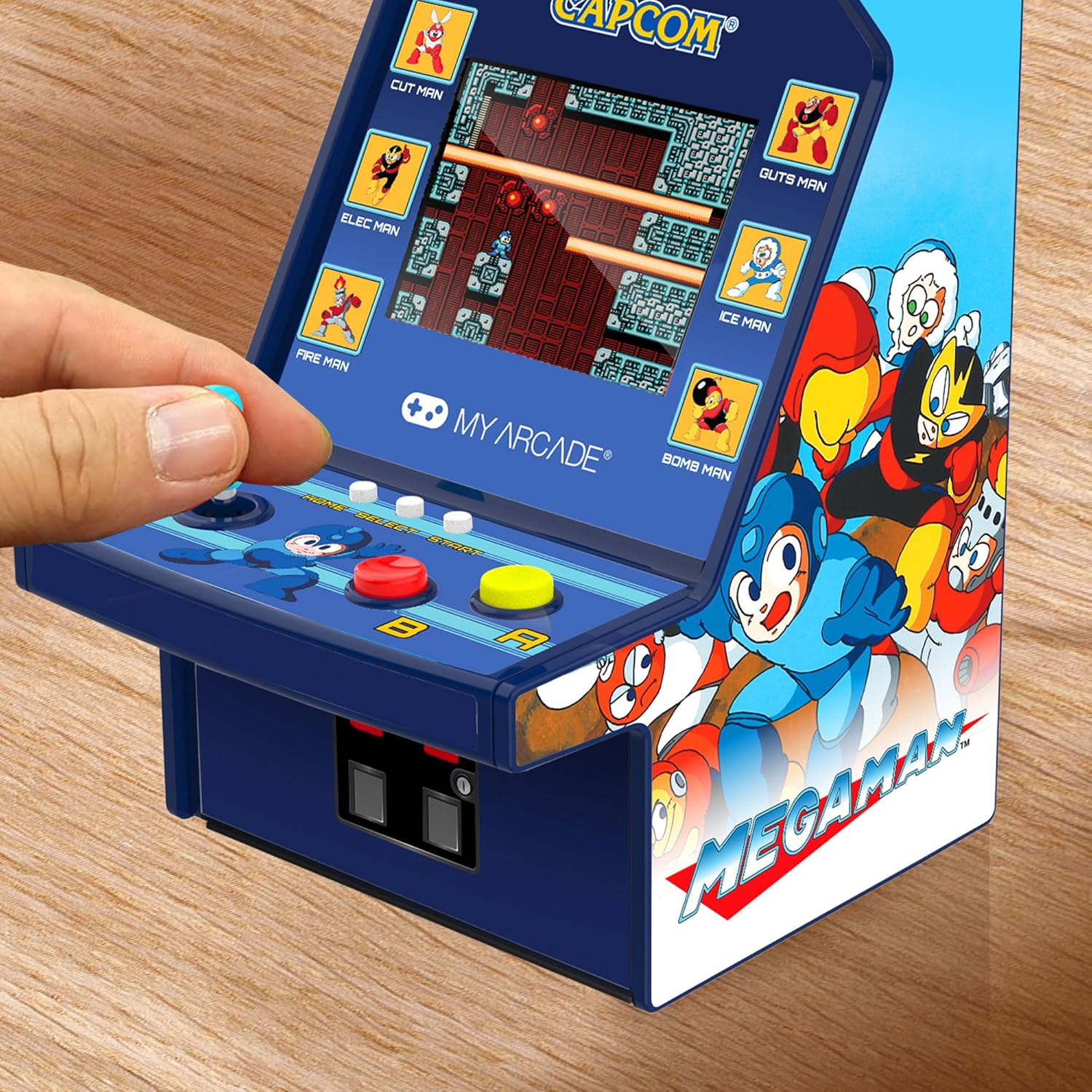 Une mini borne d'arcade avec un joystick bleu, des boutons rouges et jaunes. L'écran affiche une scène de jeu. Le côté a de l'art Mega Man.