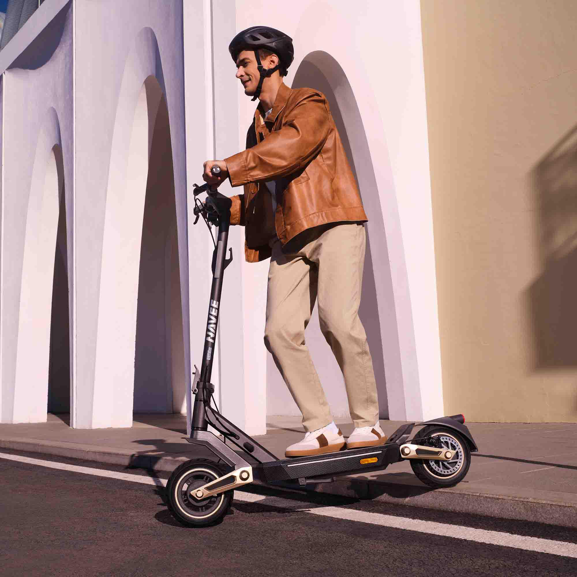Ein Mann fährt einen Elektroroller. Er trägt einen Helm, eine braune Jacke und beige Hosen. Der Roller ist schwarz und gold.