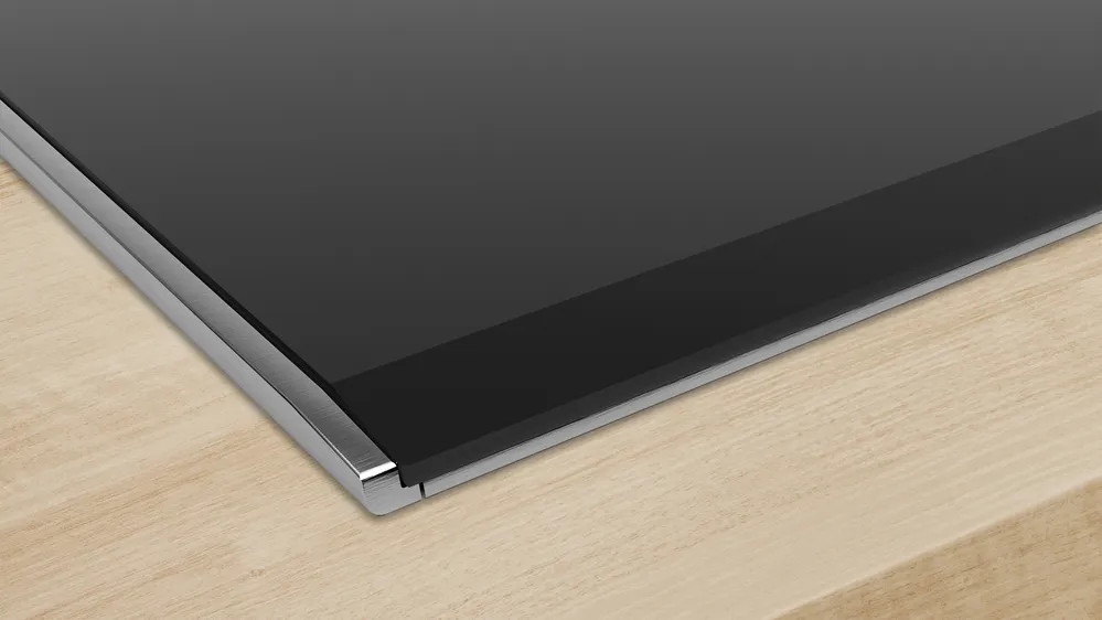 Czarna, odblaskowa powierzchnia z metalową obwódką na jasnym drewnie. Widok z bliska.