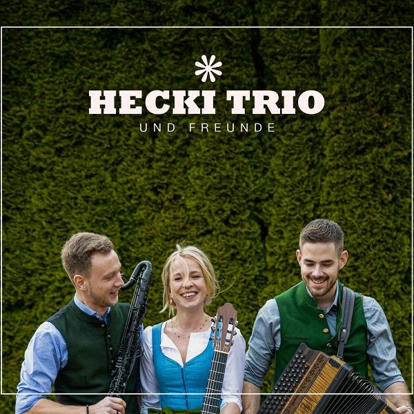 Drei Personen in Tracht posieren. Eine Frau hält eine Gitarre, ein Mann eine Klarinette und ein anderer Mann ein Akkordeon.