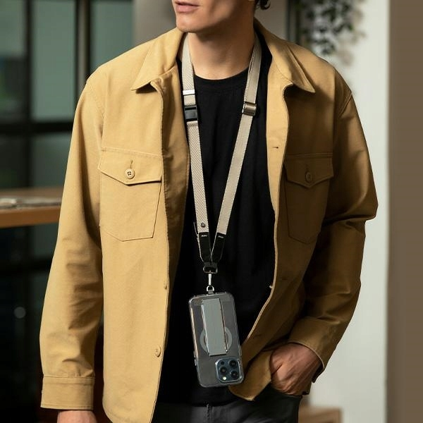 Mężczyzna w beżowej kurtce i smyczy z etui na telefon. Tło jest rozmyte, wnętrze.