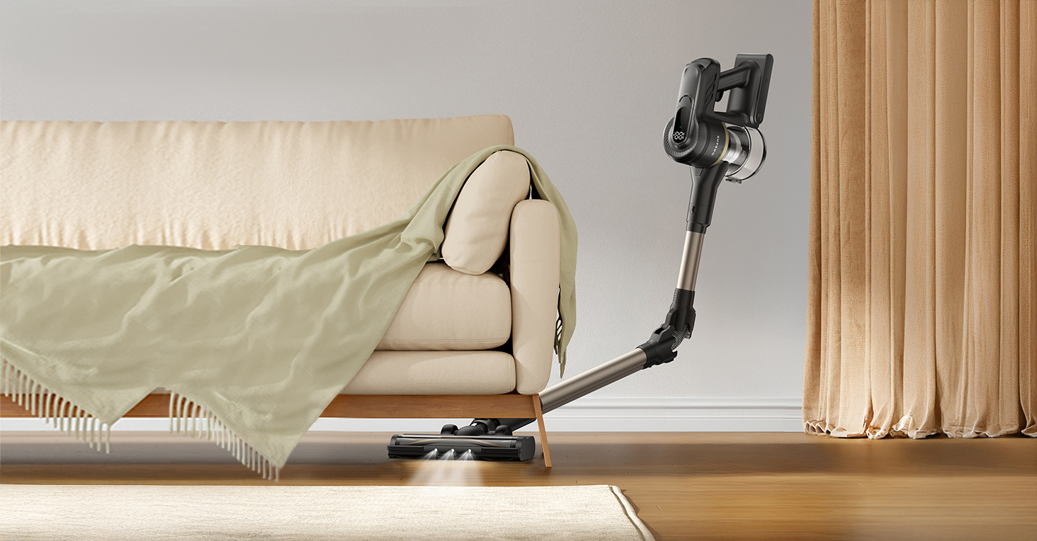 Odkurzacz bezprzewodowy obok beżowej sofy z zielonym kocem. Beżowy dywan leży na drewnianej podłodze, a w tle zasłona.