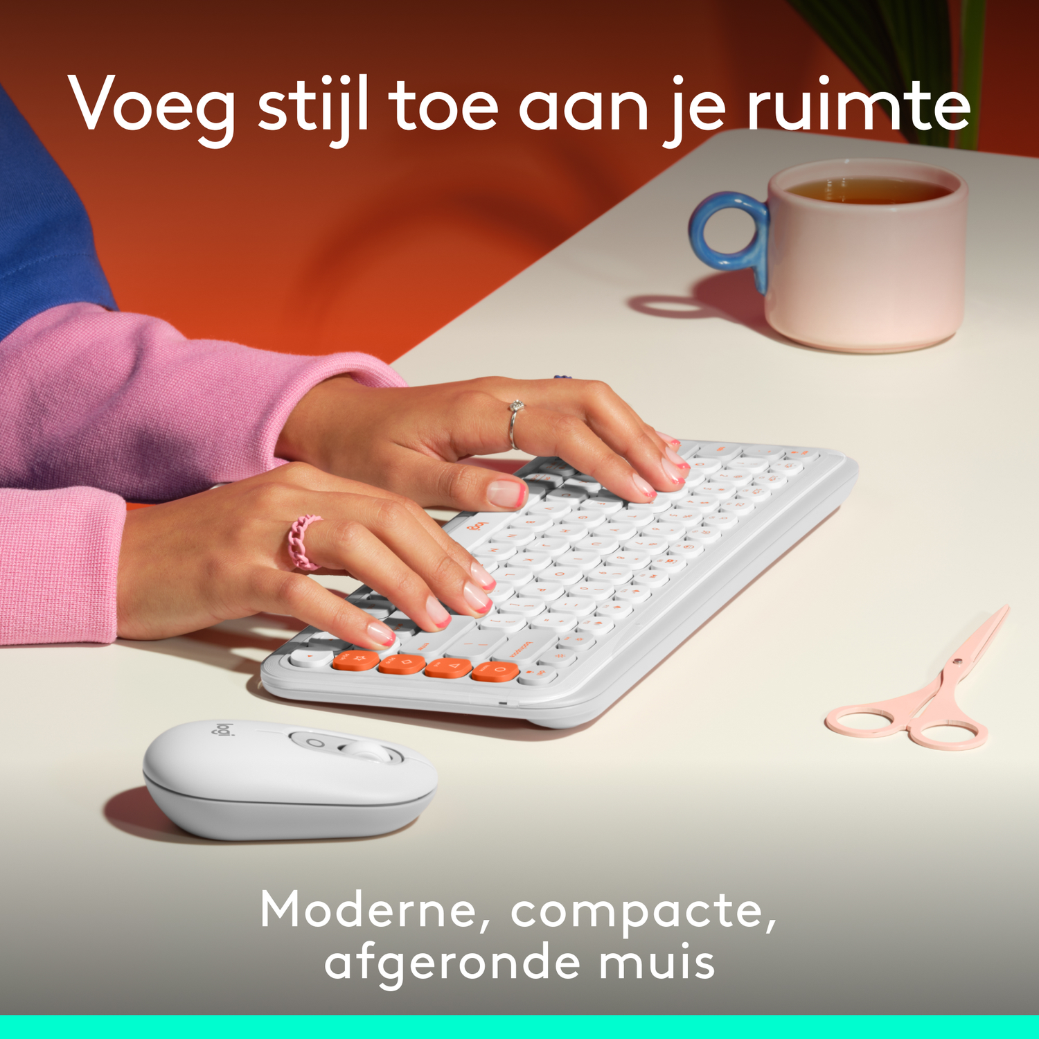 Hands typing on a white keyboard with orange keys. A white mouse, pink scissors, and a pink mug with tea are on the table.