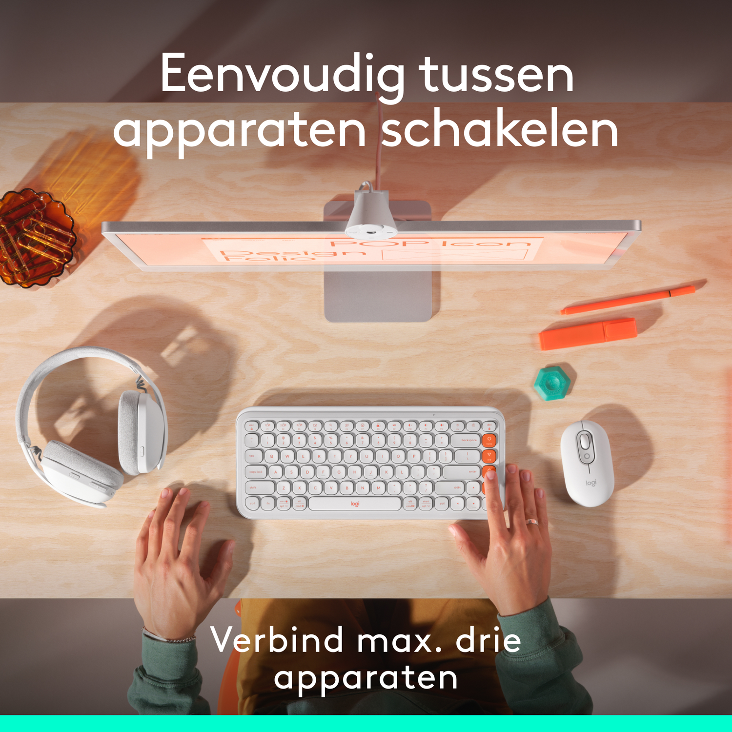 A desk setup with a monitor, keyboard, mouse, and headphones. A hand is on the keyboard. The background is a wooden desk.