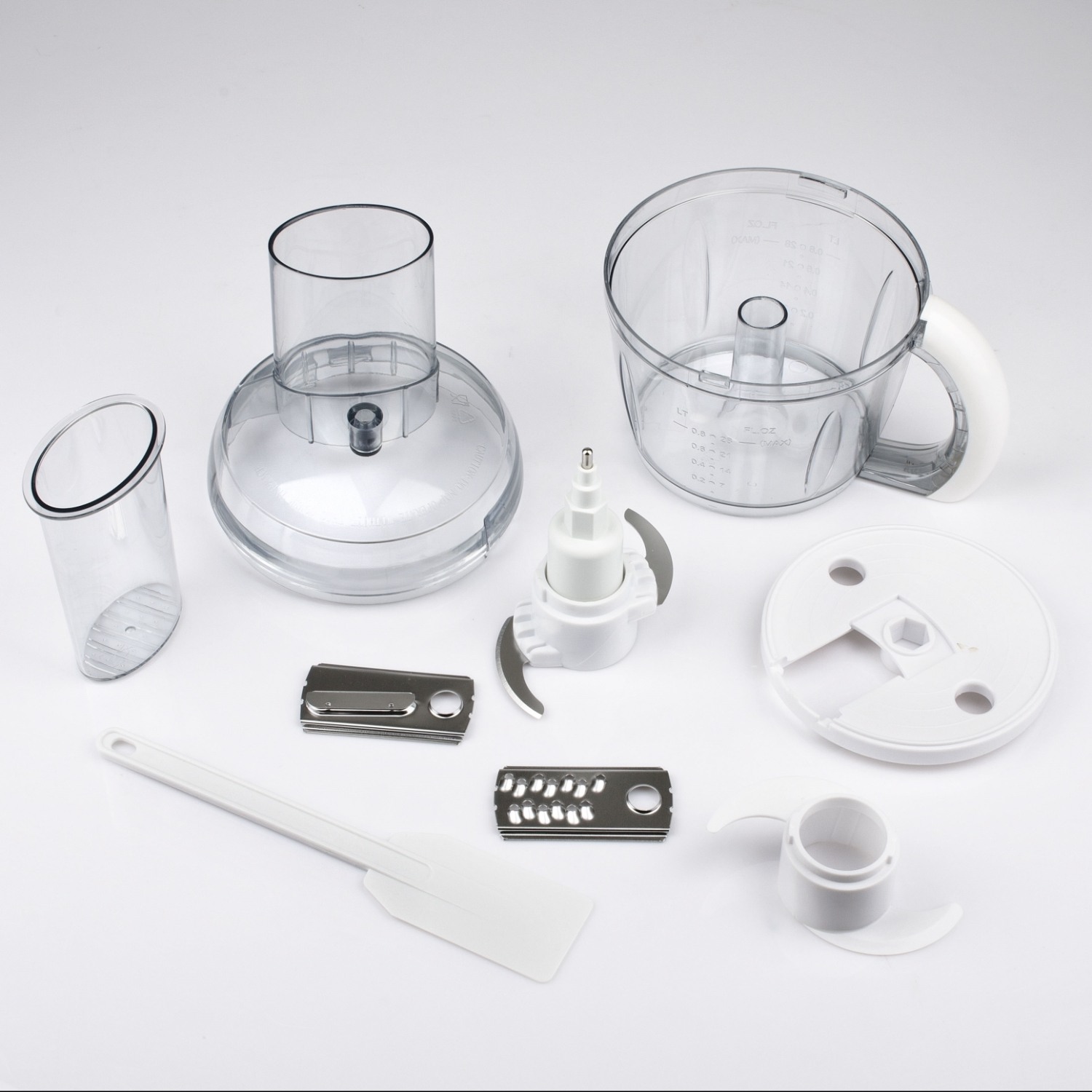 Un robot da cucina smontato su una superficie bianca. Include ciotole di plastica trasparente, lame bianche, un manico bianco e una spatola bianca.