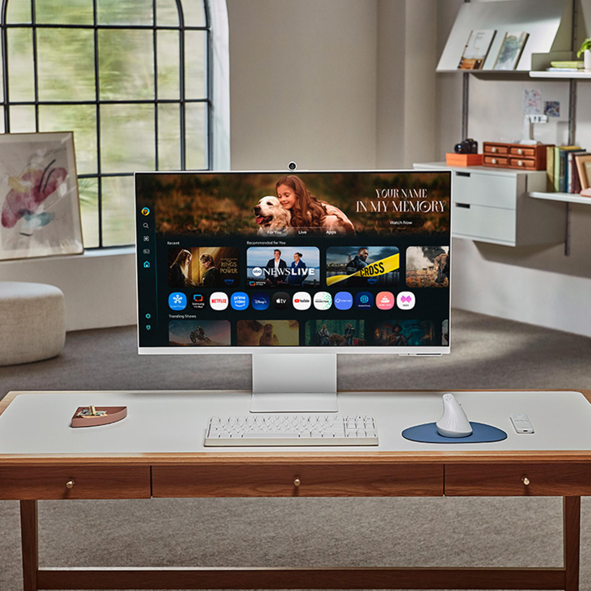Ein moderner Schreibtisch mit einem großen Monitor, auf dem ein Film gezeigt wird. Auf dem Schreibtisch liegen eine Tastatur, eine Maus und eine Fernbedienung.