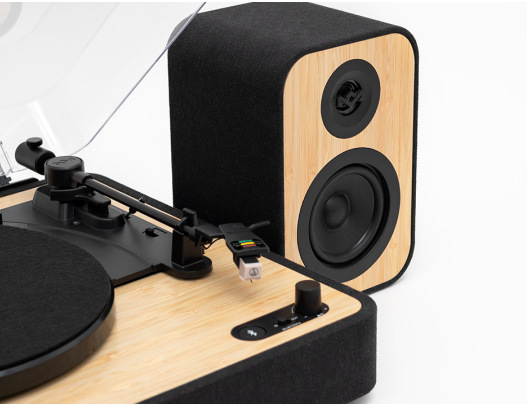 Gramofon z głośnikiem. Gramofon ma drewnianą podstawę, czarne ramię i osłonę. Głośnik jest czarny i w kolorze drewna.