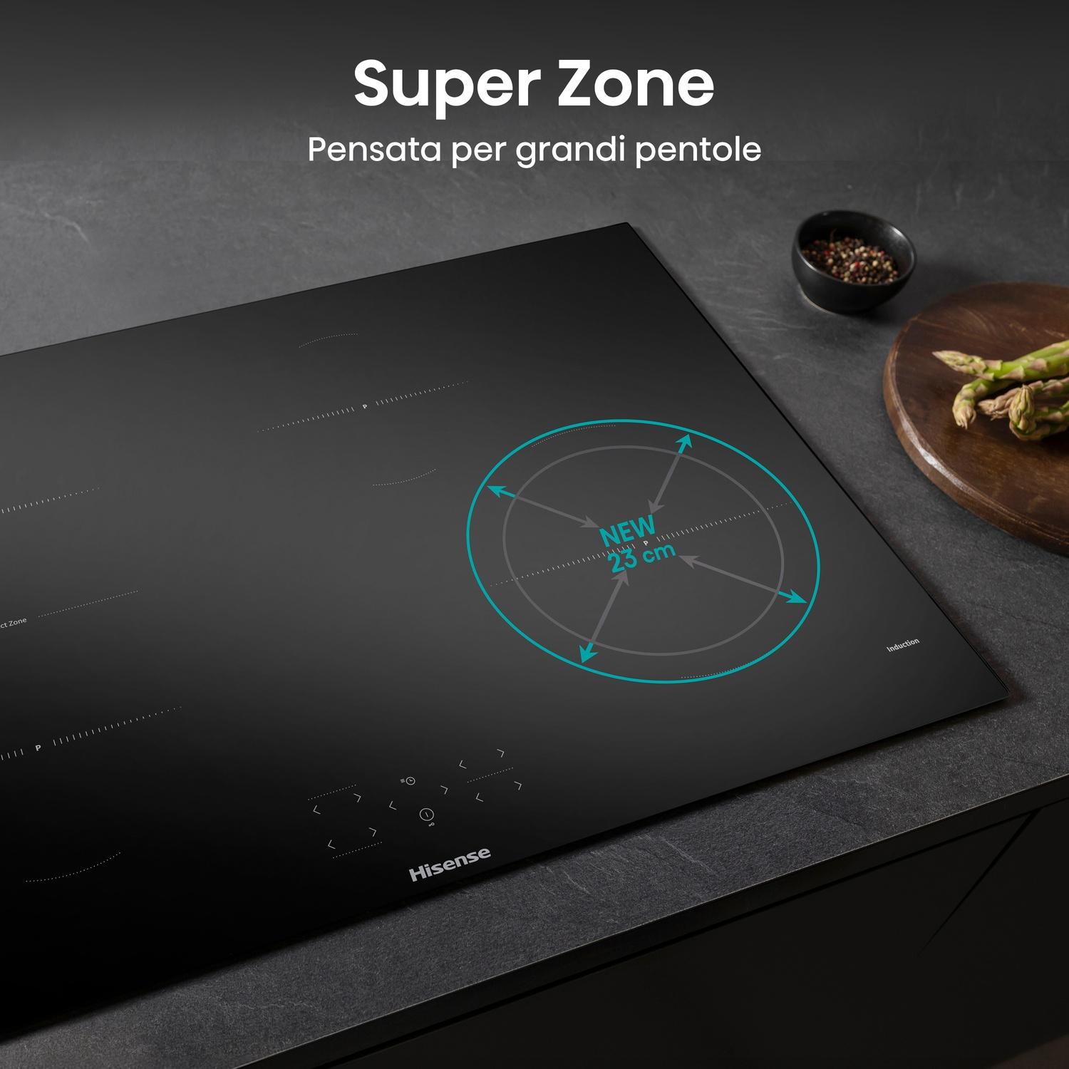 Un piano cottura a induzione nero con una zona evidenziata, il testo recita 'Super Zone'. Una ciotola di spezie e asparagi sono sul lato.