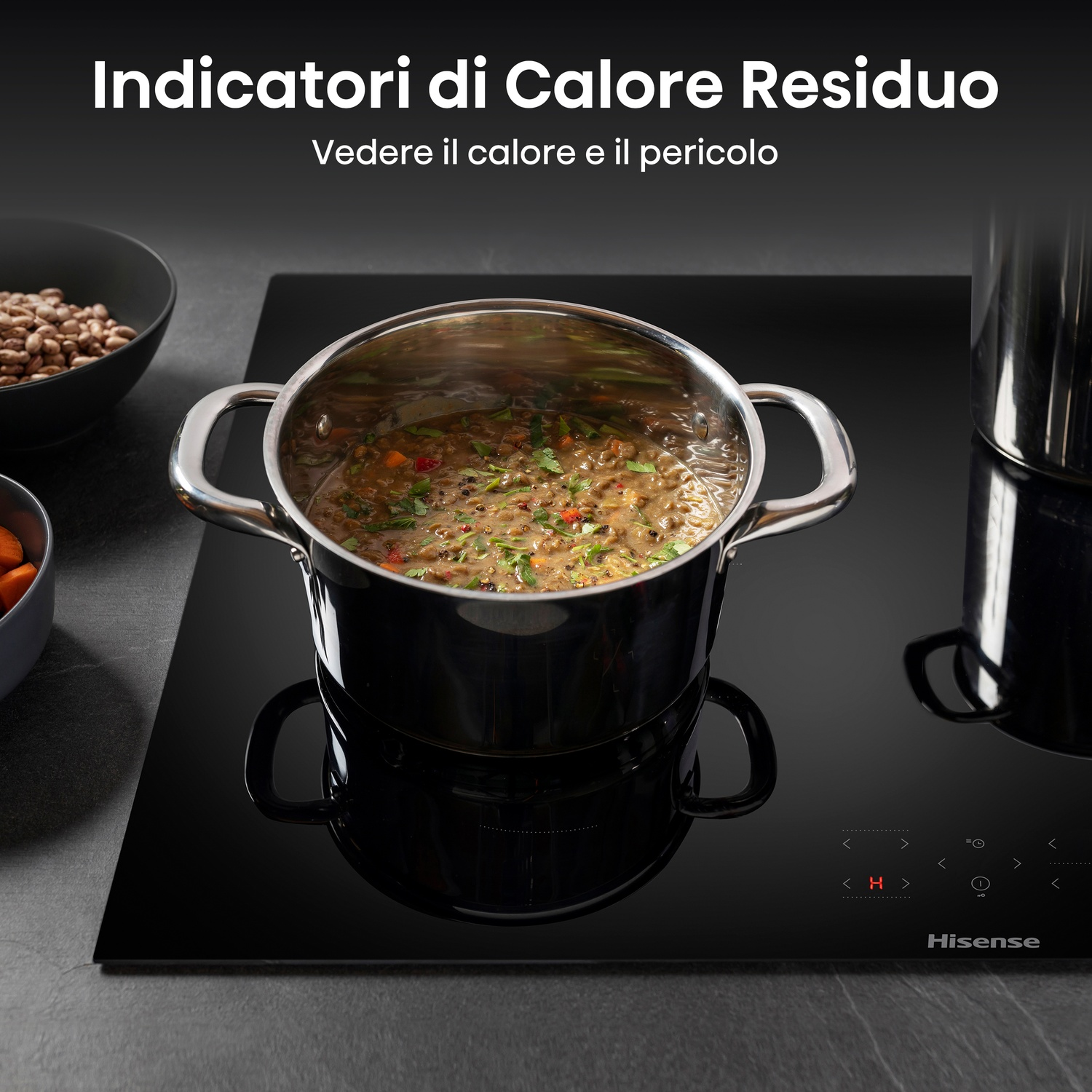 Una pentola di stufato sobbolle su un piano cottura a induzione nero. Sale vapore. Ci sono ciotole di verdure nelle vicinanze.