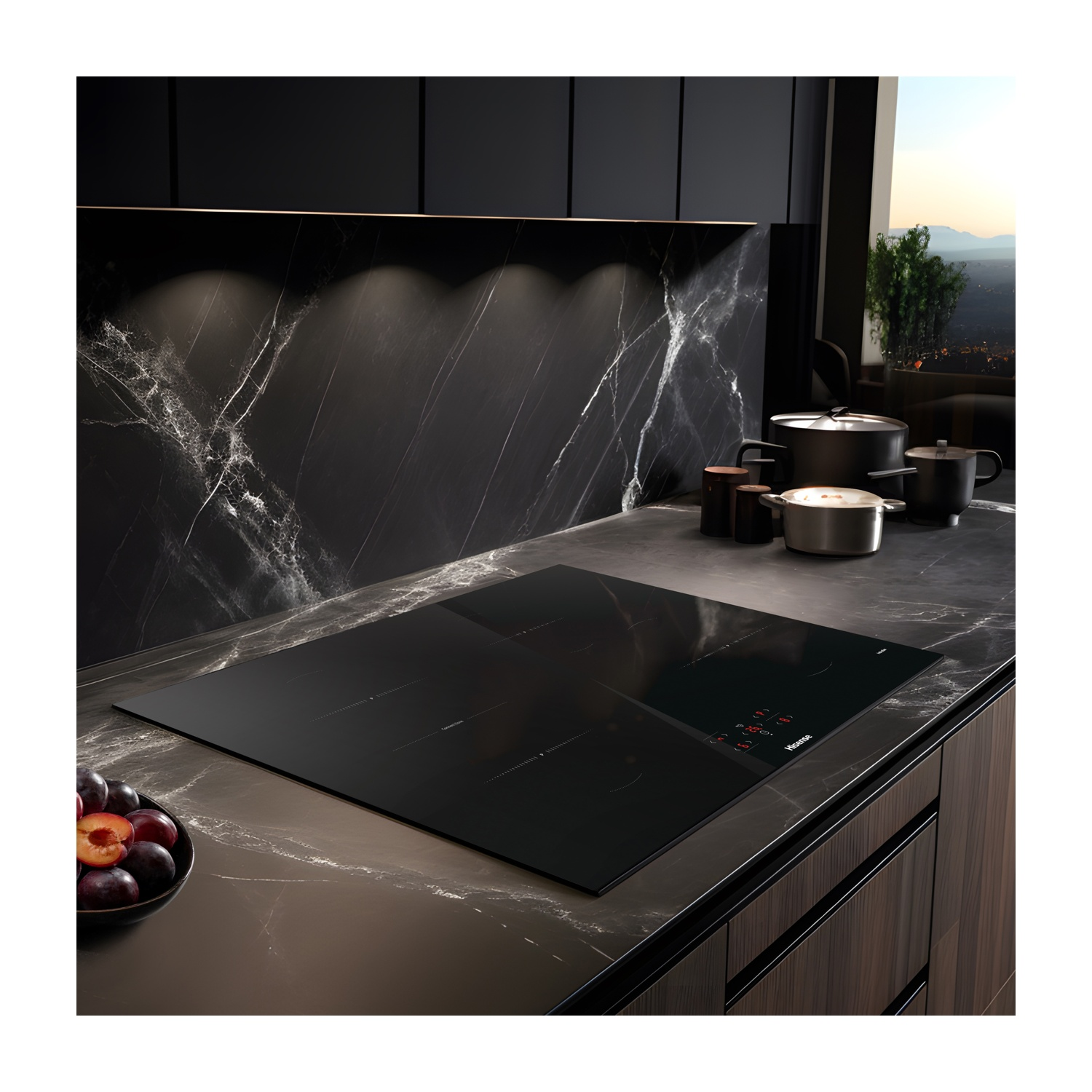 Una cucina moderna con piano cottura a induzione nero, pentole e una ciotola di prugne. Schienale in marmo e mobili in legno.