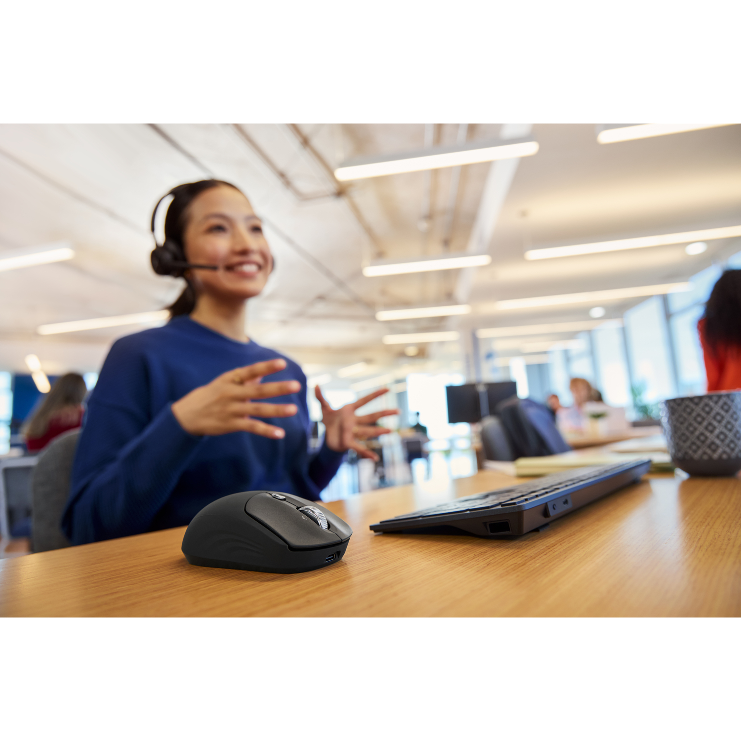 Femme avec casque gestuelle, avec souris et clavier sur le bureau. Autres personnes au bureau. Accent sur le bureau.
